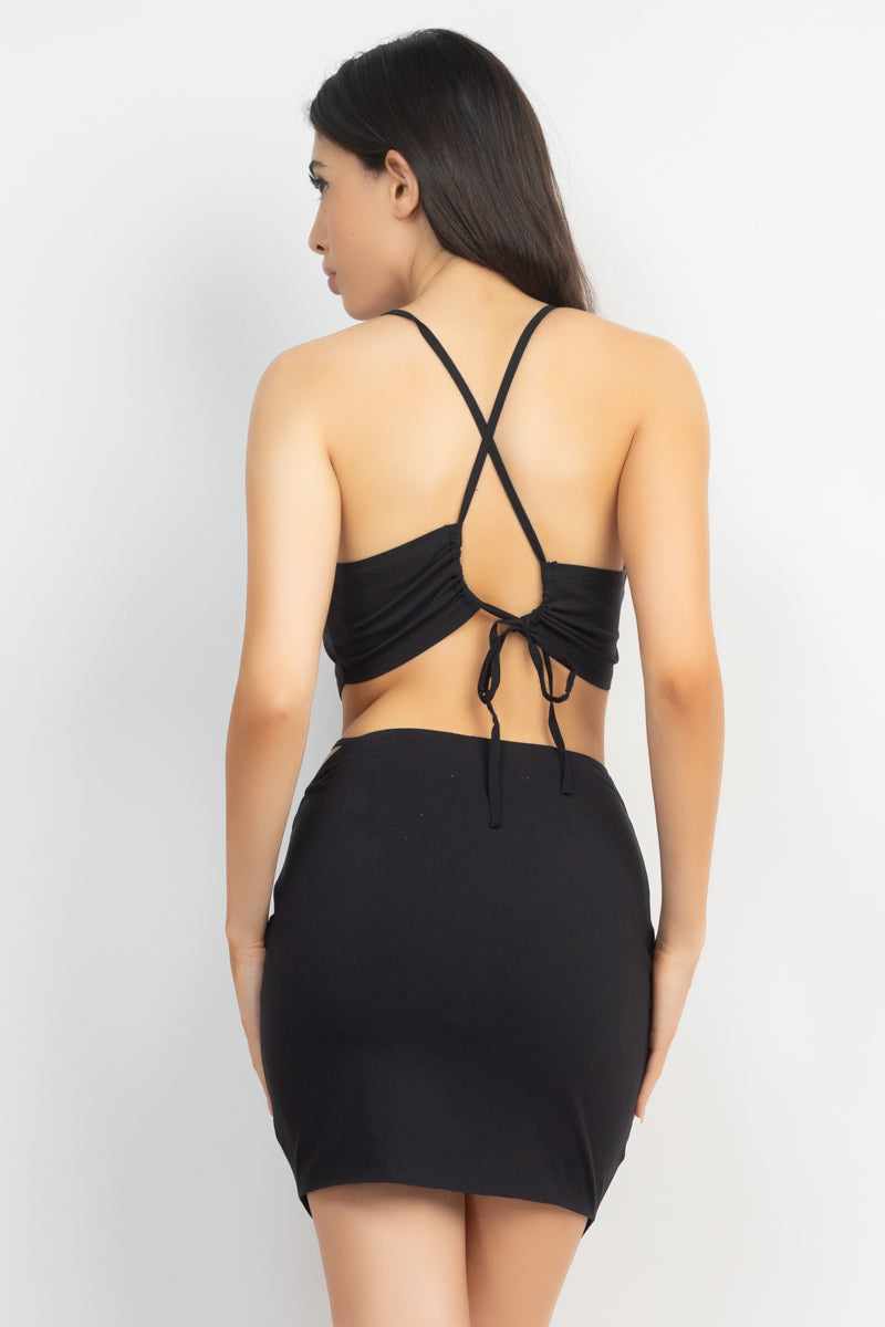 Black asymmetrical cross back top and skirts set with drawstring detail and side cutouts, made from rayon, nylon, and spandex blend.