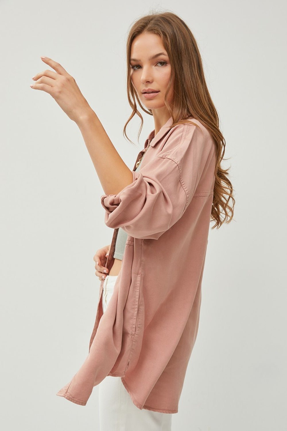 Woman wearing a stylish pink button-up long sleeve denim shirt made from 100% tencel fabric with a relaxed fit and no stretch.