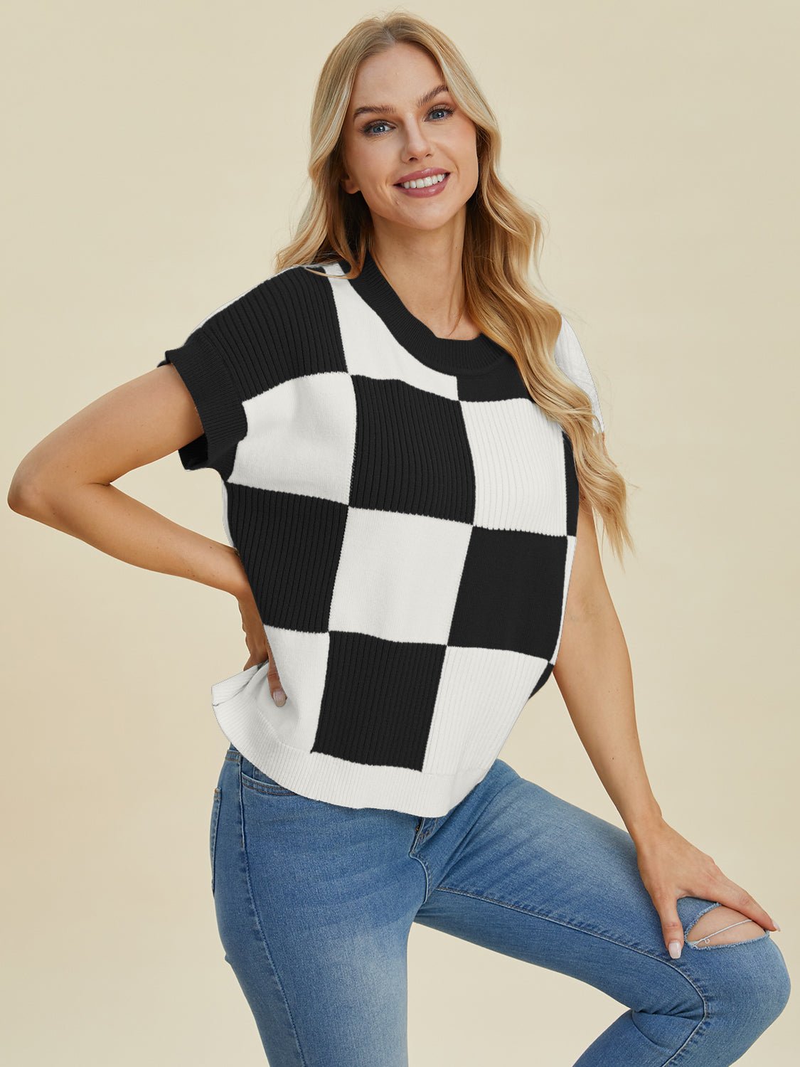 Woman wearing checkered round neck short sleeve sweater, black and white design, styled with blue jeans.