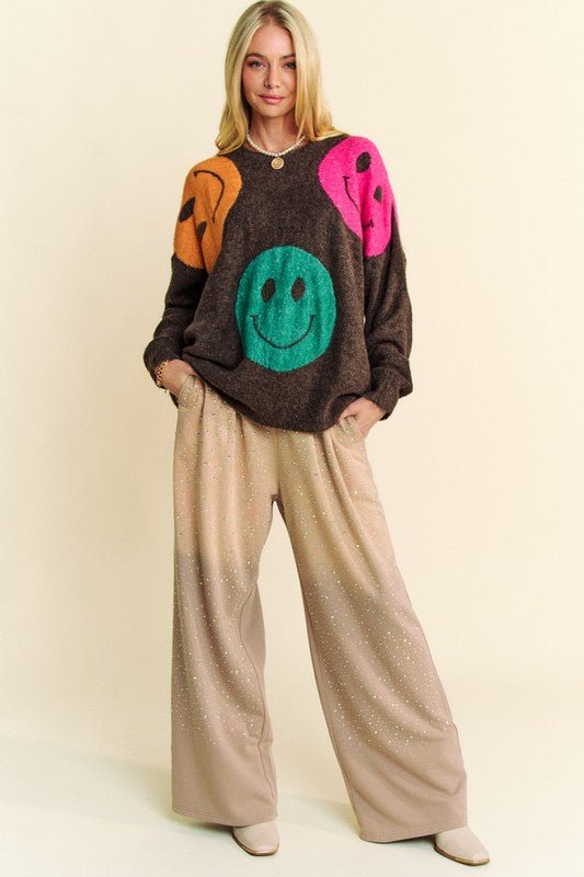Woman wearing a Contrast Smile Round Neck Oversize Sweater with colorful smiley faces, paired with beige wide-leg pants.