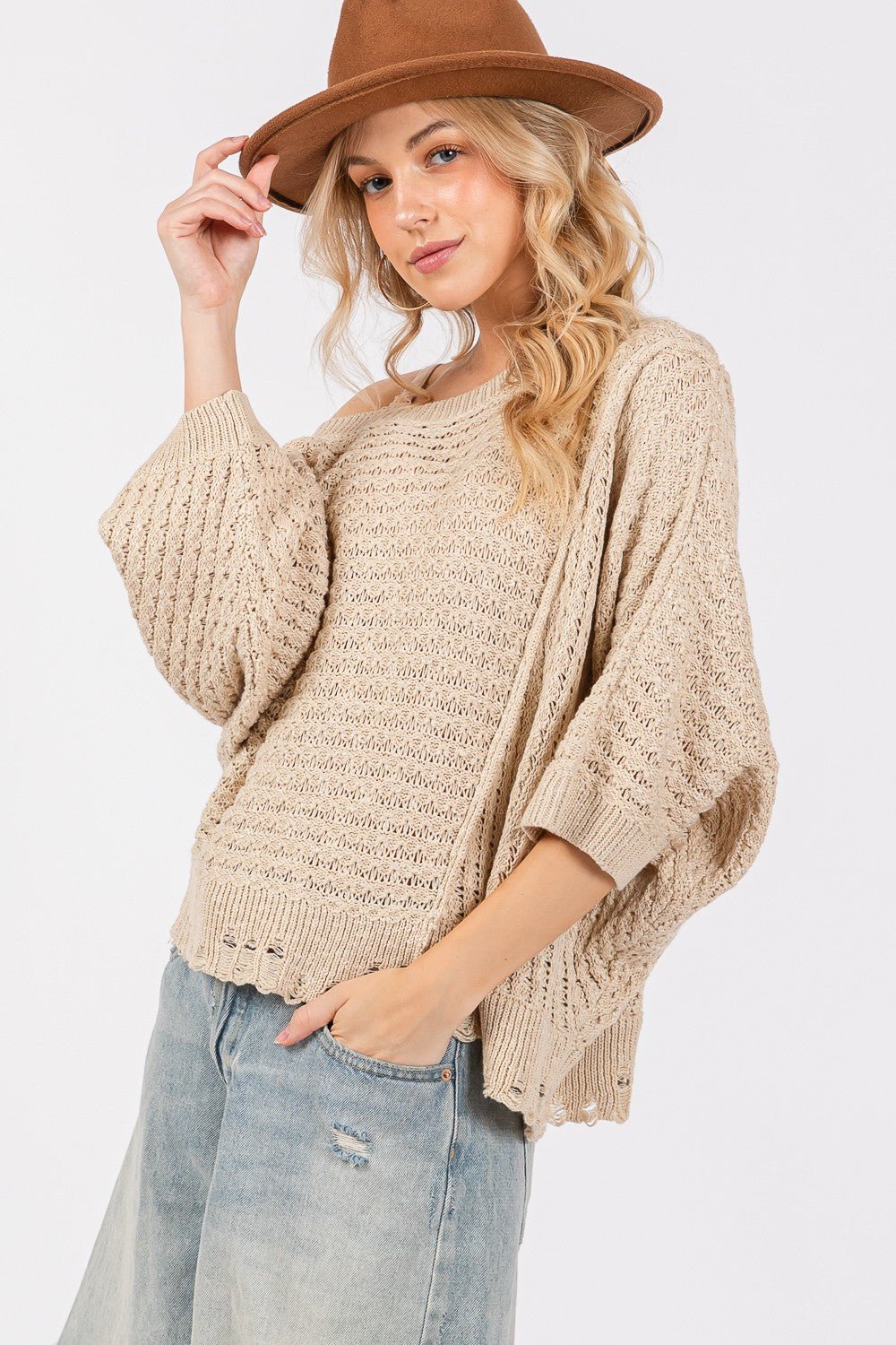 Woman wearing a distressed asymmetrical open stitch sweater with a hat and jeans.