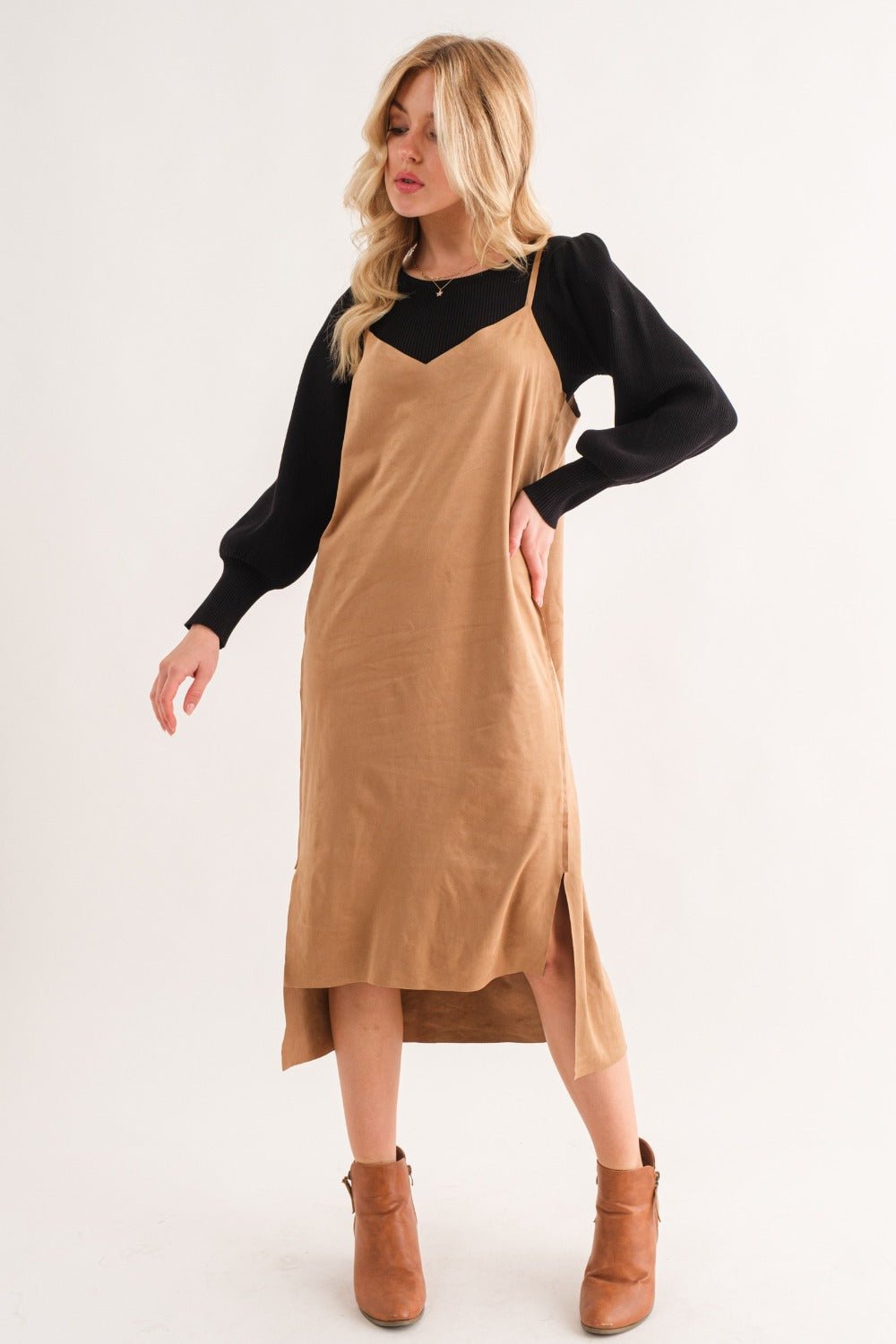 Woman wearing a Faux Suede Cut Edge Slit Cami Midi Dress in tan with high-low hem, styled over a black top and ankle boots.