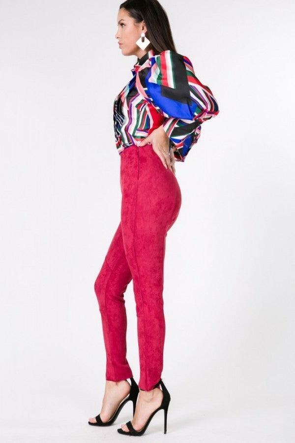 Woman wearing deep red faux suede skinny pants paired with a colorful striped blouse and black high heels.