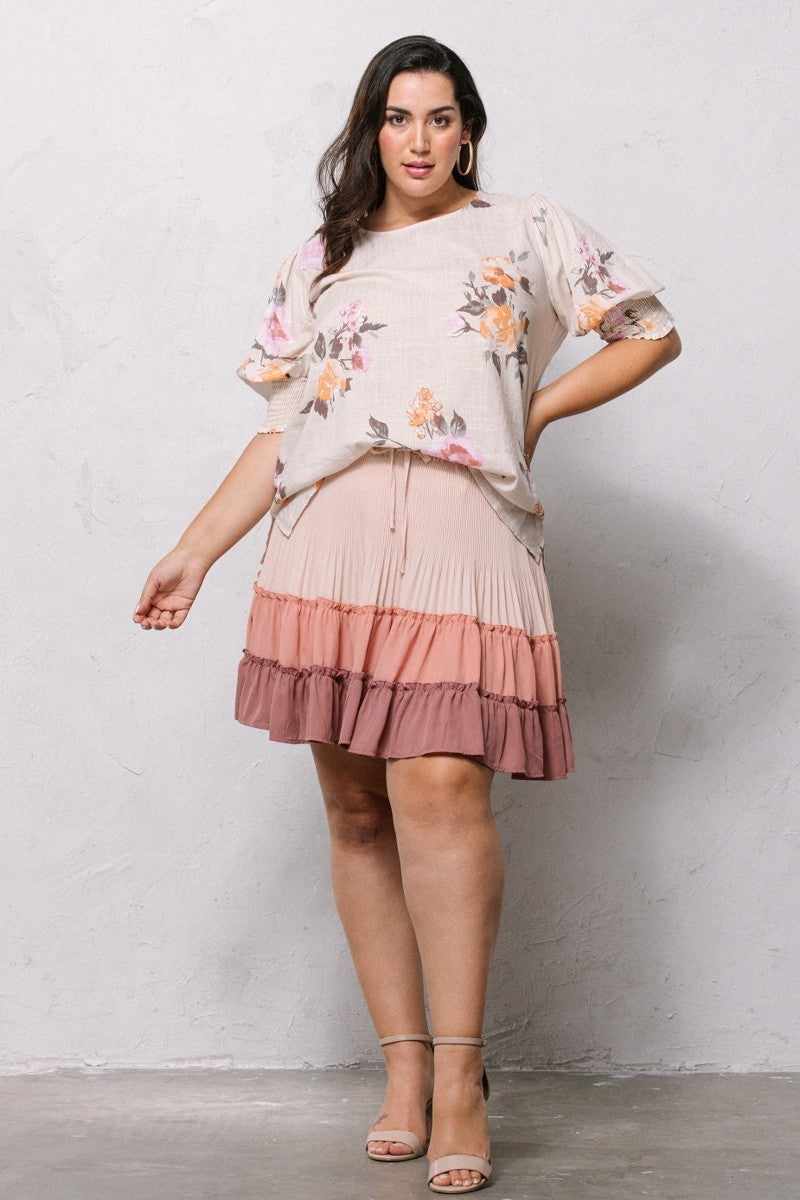 Woman wearing a floral printed blouse with puffed sleeves and a tiered skirt, posing against a light gray background.