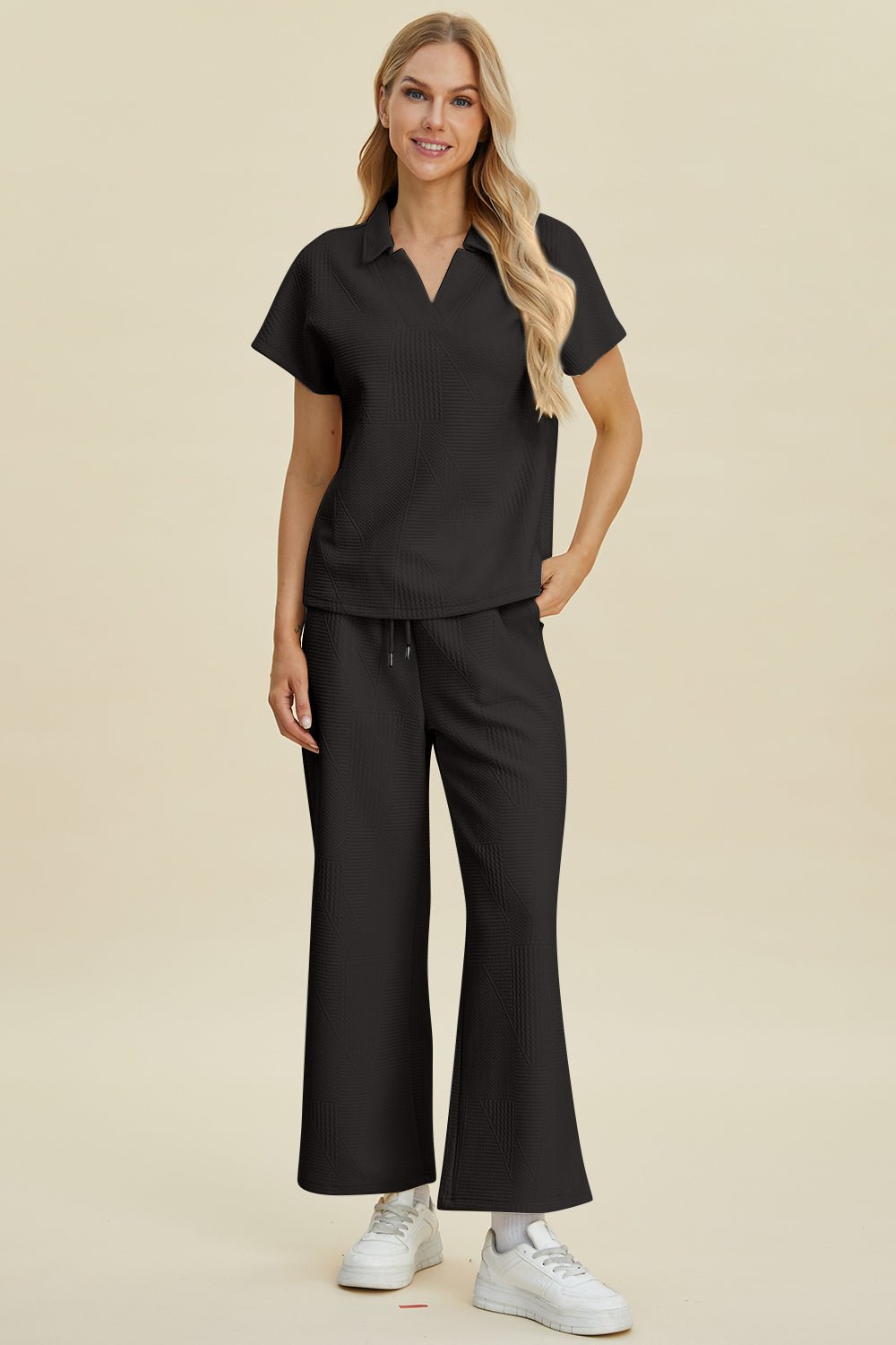 Woman wearing a full size collared neck short sleeve top and pants set in black, made of slightly stretchy polyester and elastane.