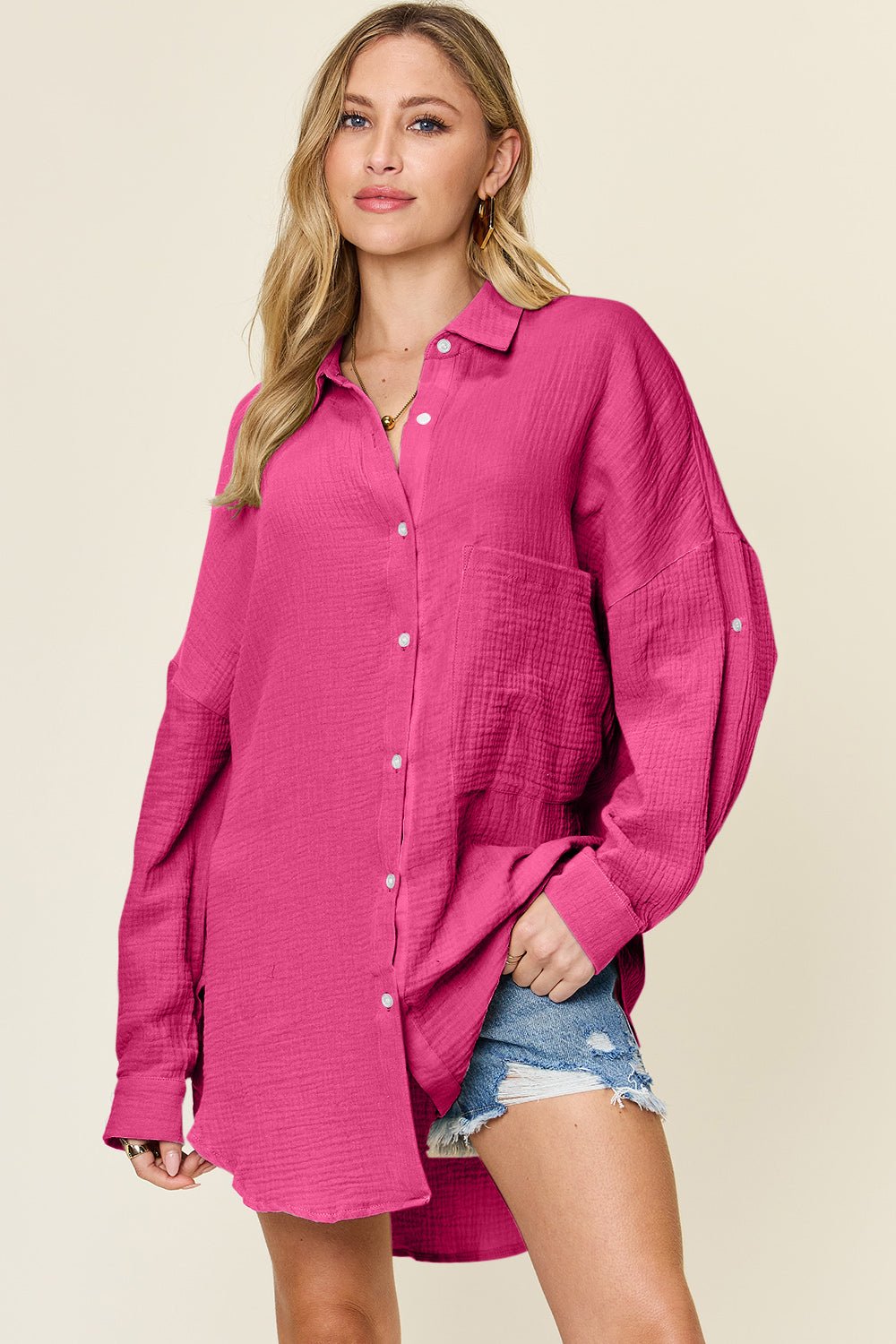 Woman wearing full size pocketed texture button-up shirt in pink with denim shorts.