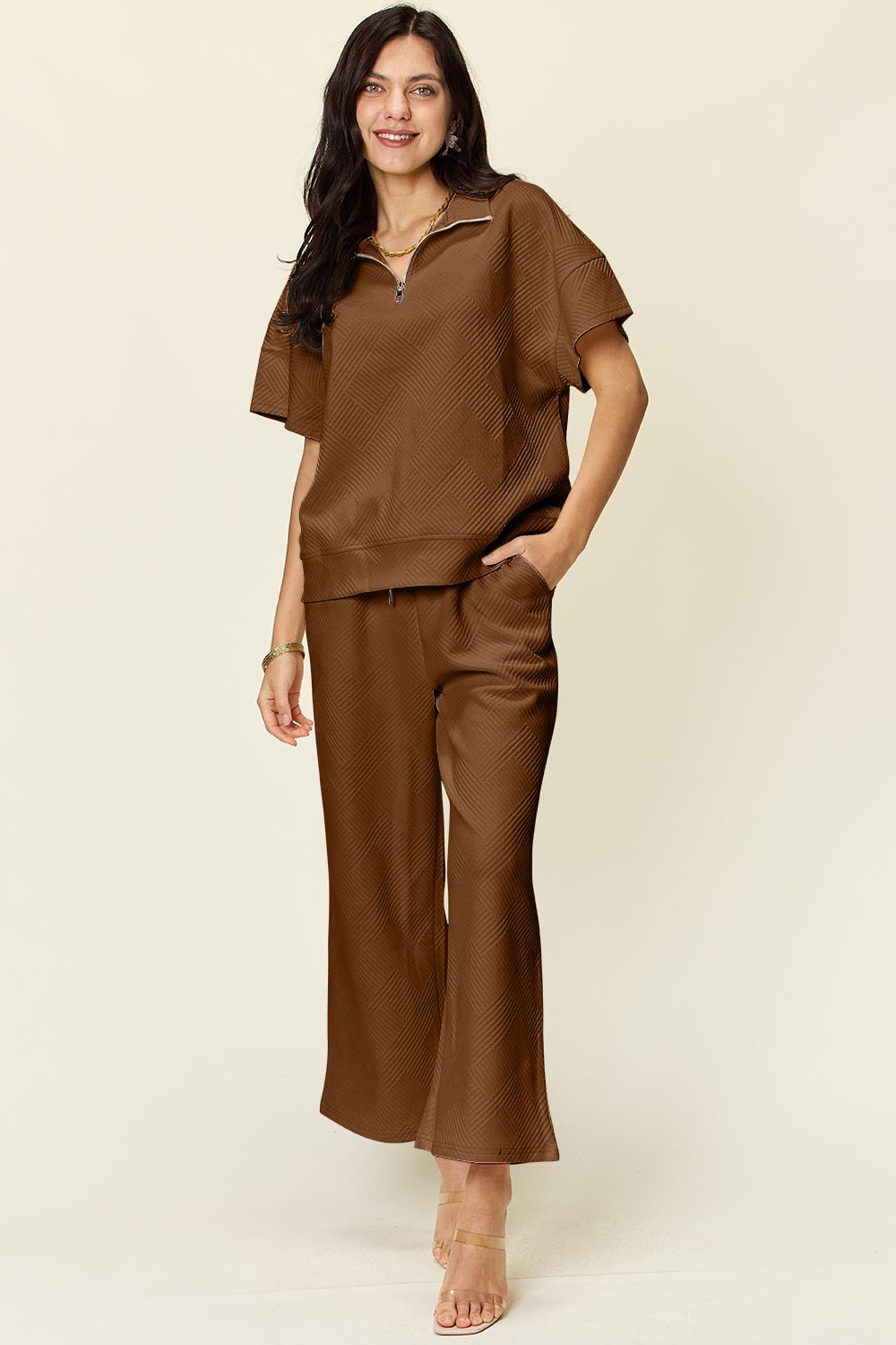 Woman wears brown two-piece texture half zip short sleeve top and pants set with pockets, featuring slightly stretchy polyester-spandex fabric.