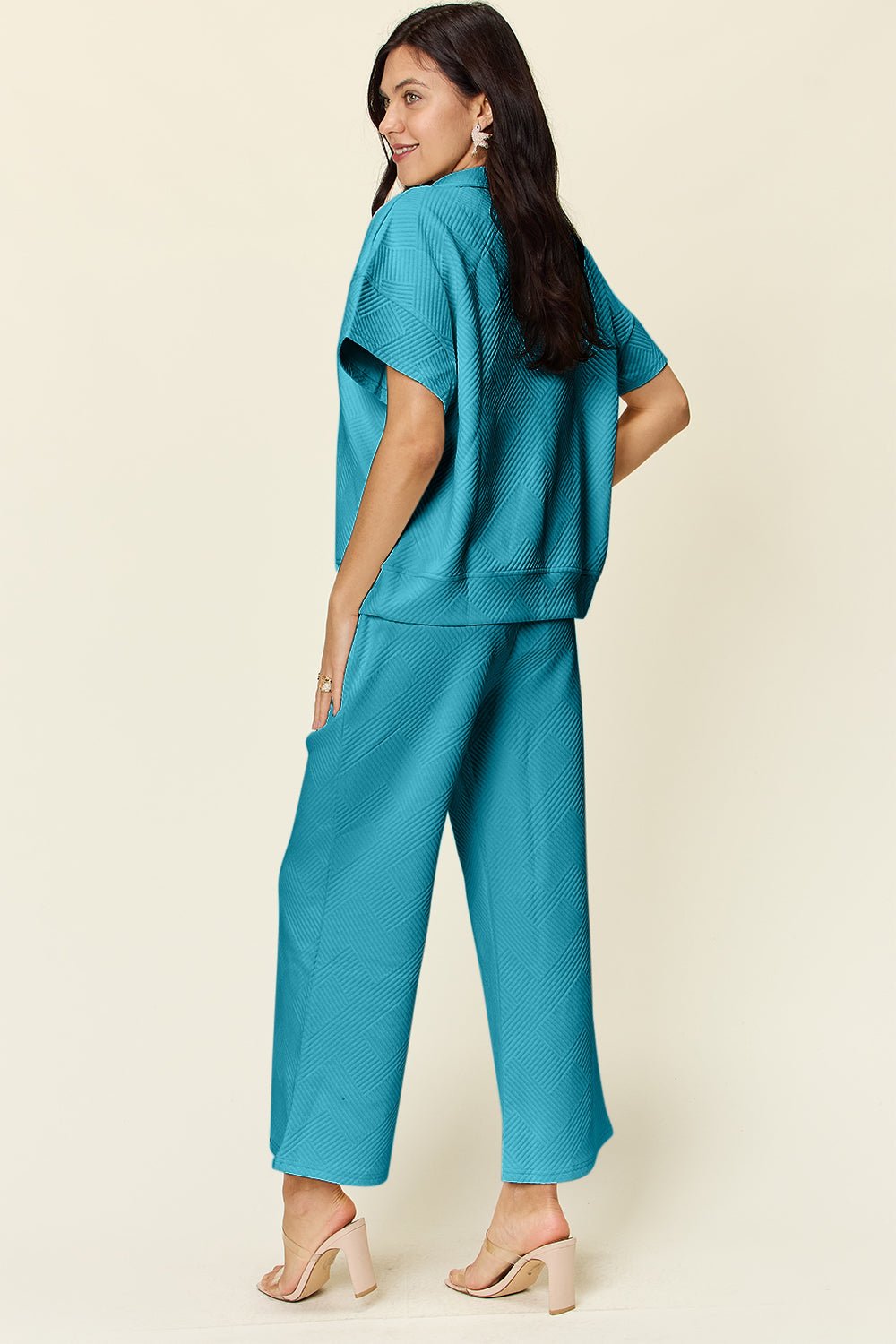 Woman wearing teal full size texture half zip short sleeve top and pants set with pockets and drawstring, two-piece outfit.