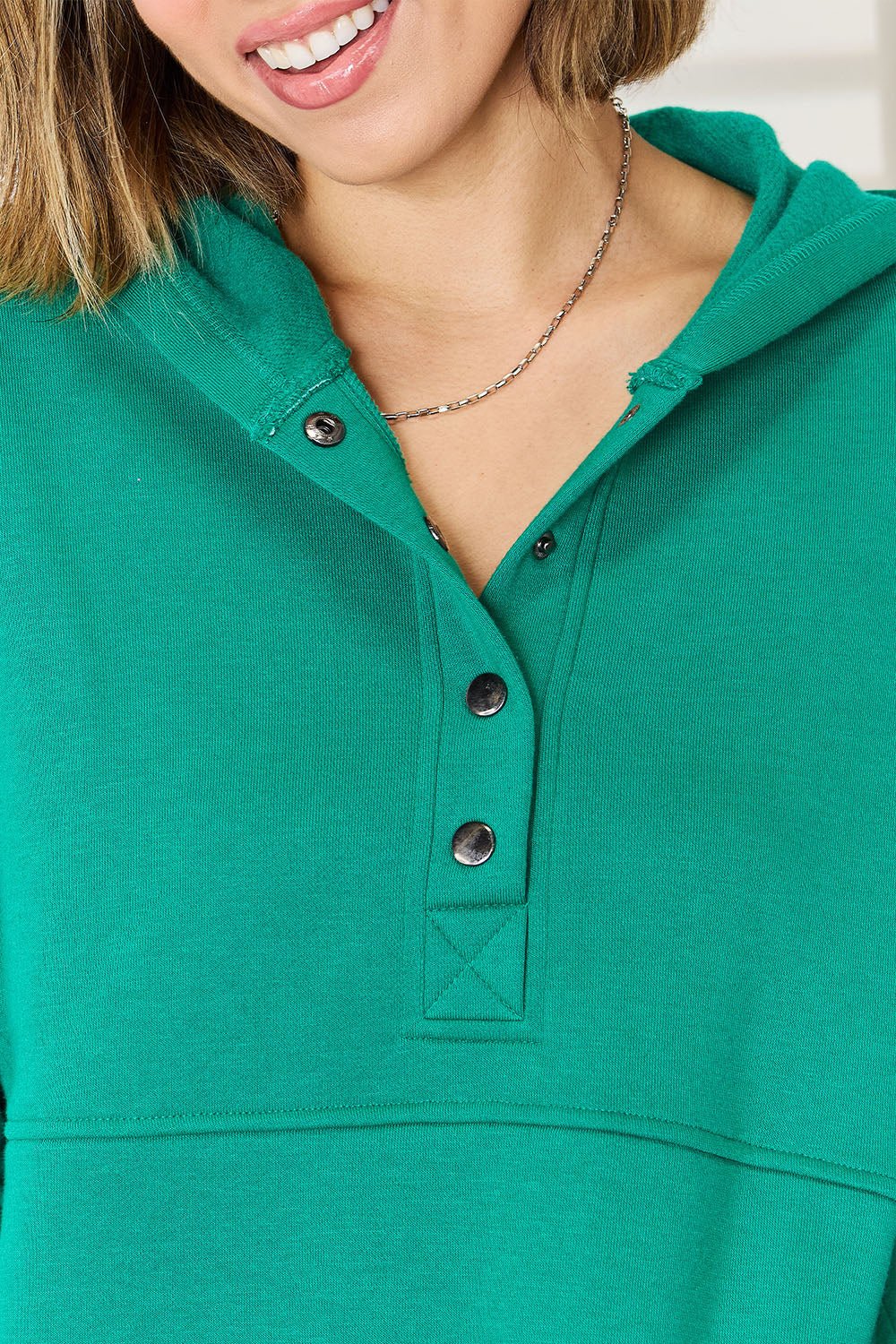 Woman wearing a green half snap long sleeve hoodie made of 60% cotton and 40% polyester.