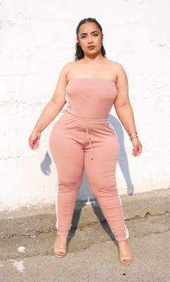 Woman wearing a strapless pink jumpsuit standing against a white wall.