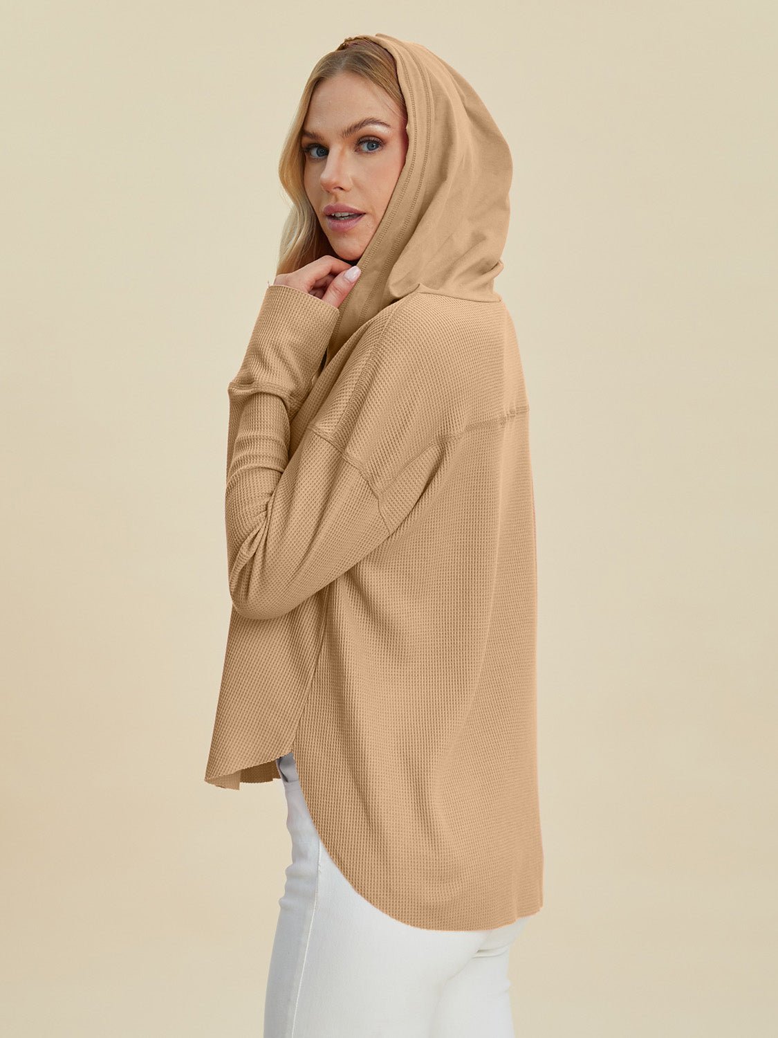 Woman wearing a high-low dropped shoulder long sleeve hoodie in beige, showcasing a casual and stylish look with white pants.