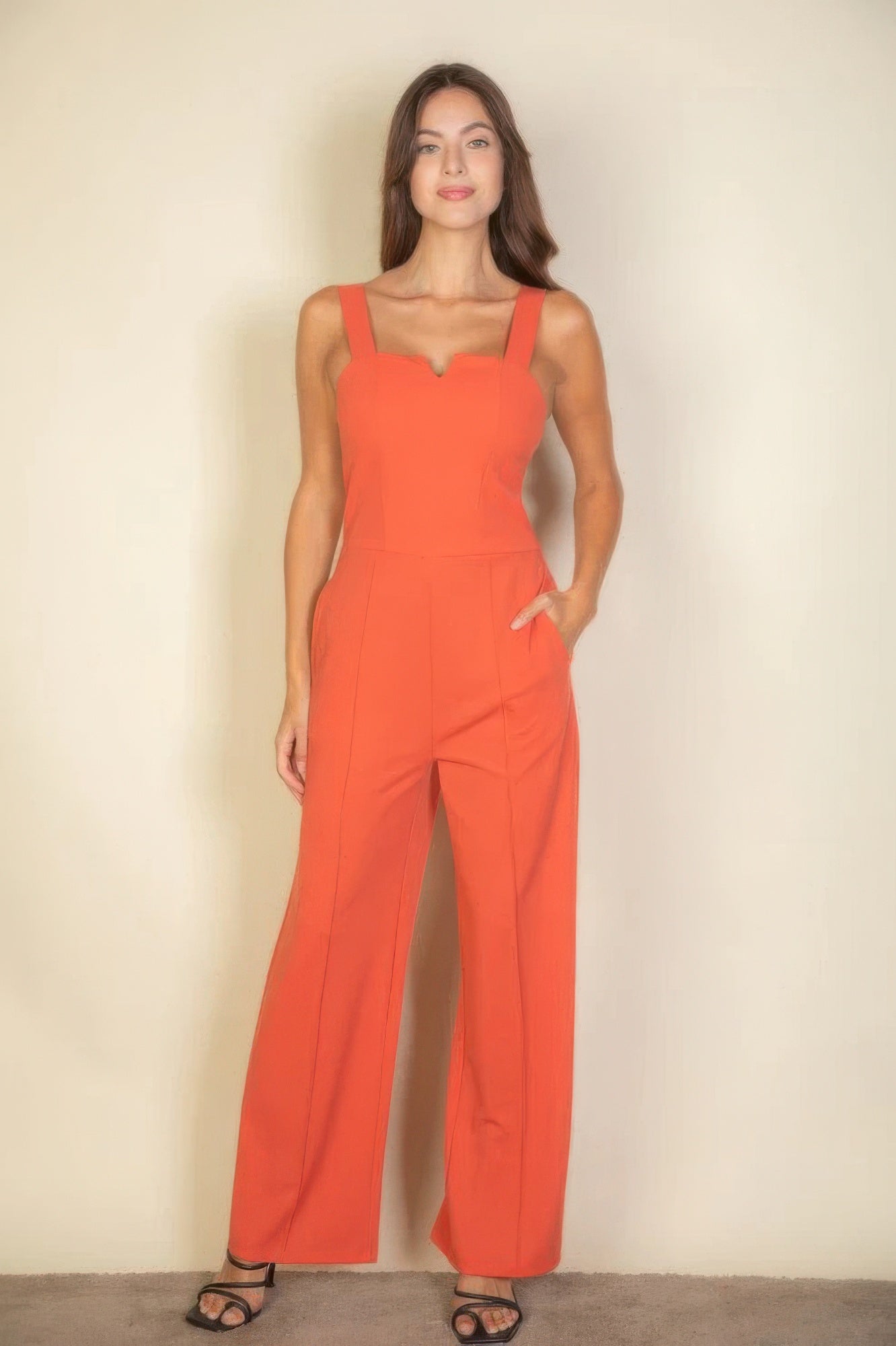 Woman wearing a chic notched neck cami jumpsuit in vibrant orange with sleek fit, perfect for versatile and stylish all-day wear.