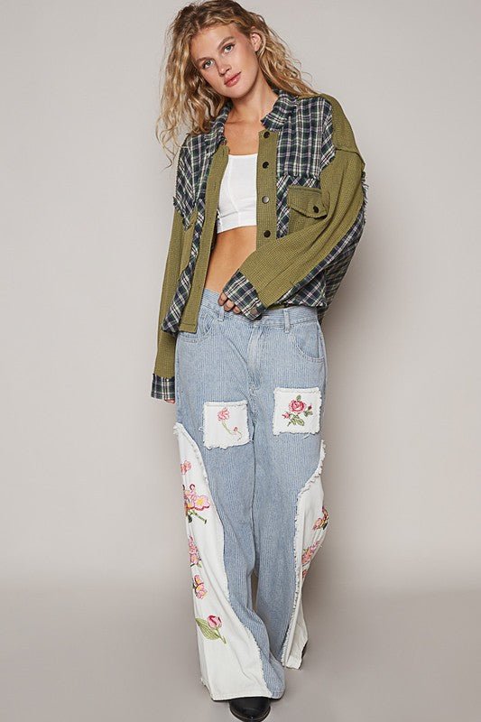 Woman wearing olive plaid button down shirt with chest pockets and floral patched denim jeans, showing trendy casual style.