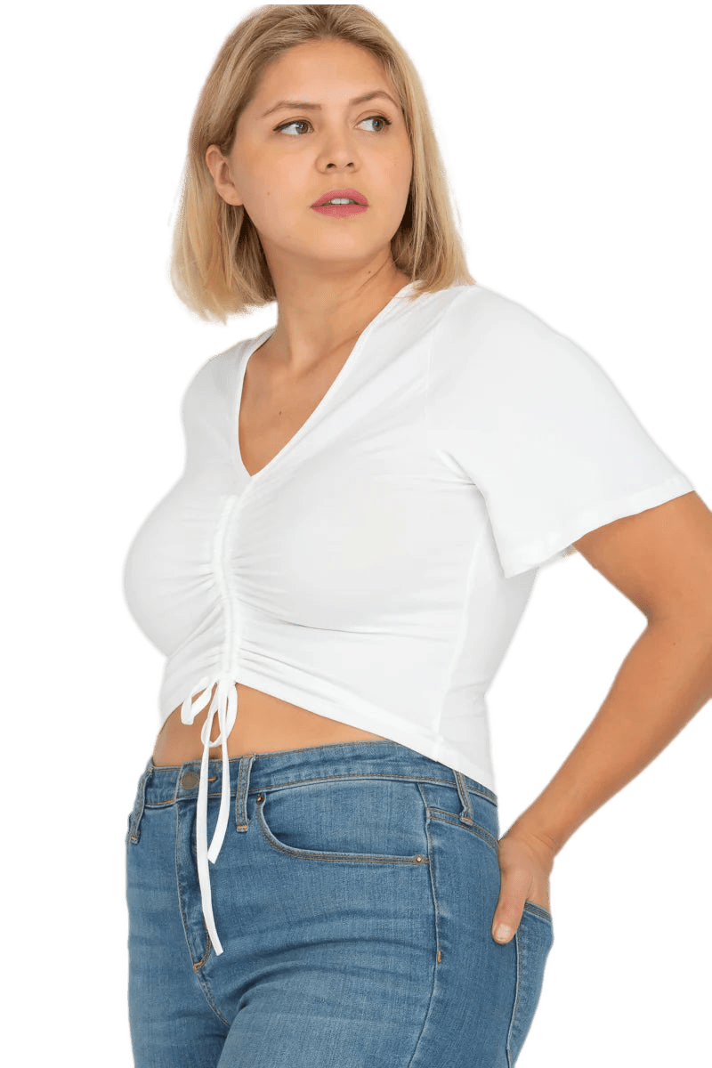 Plus size model wearing a white strap ruched front short sleeve crop top with flared sleeves and blue jeans.