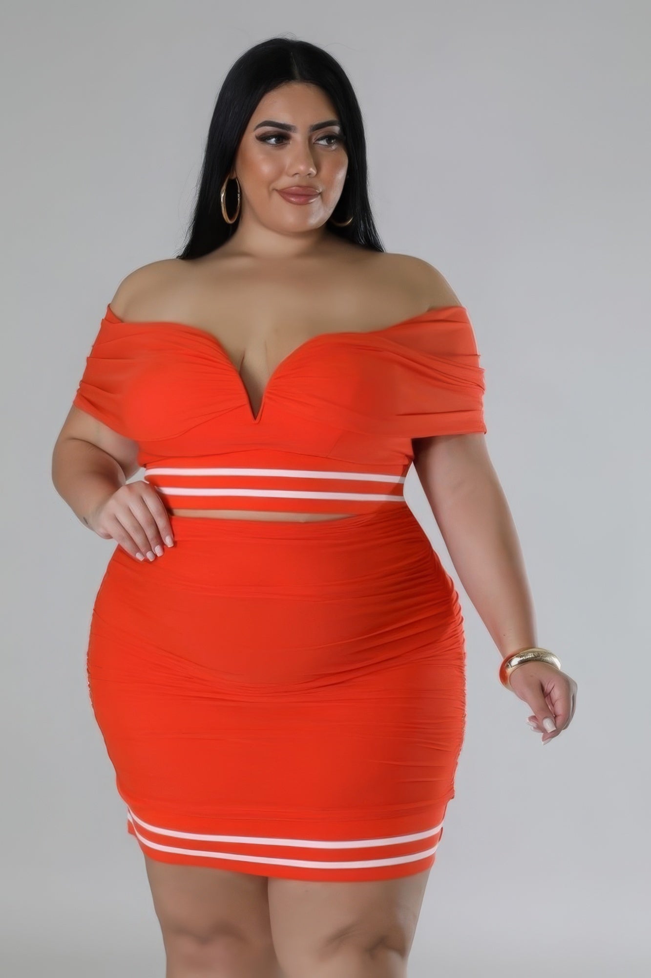 Plus size orange stretch skirt set with off-the-shoulder top, V-cut neckline, high-waisted skirt, and mesh accents on model.