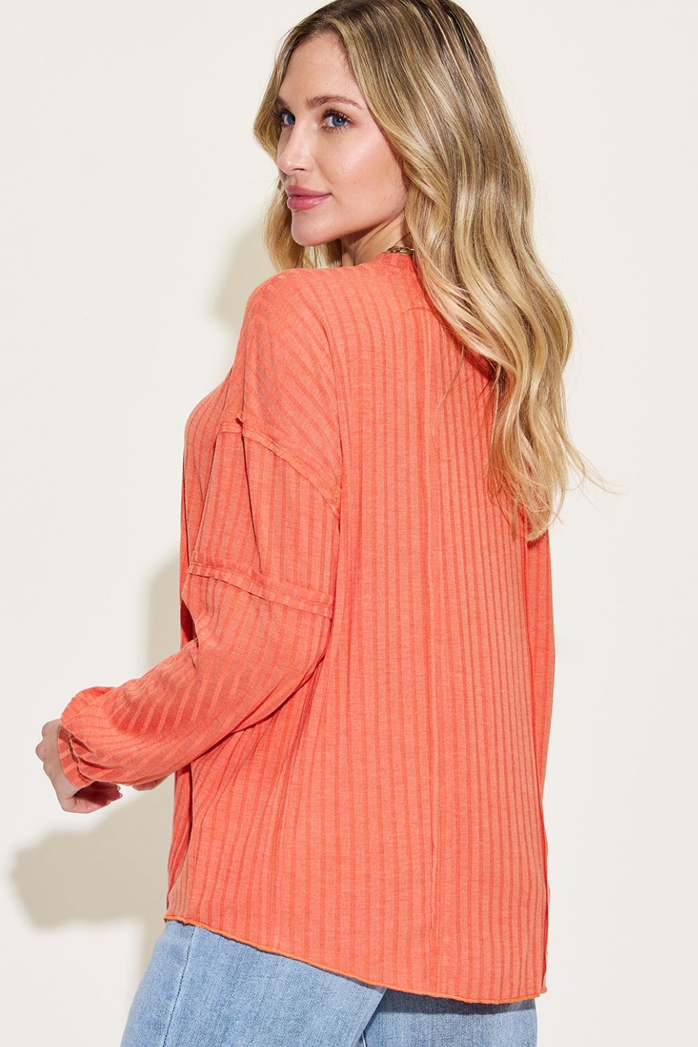 Woman wearing orange ribbed round neck long sleeve T-shirt with exposed seams, showing back view.