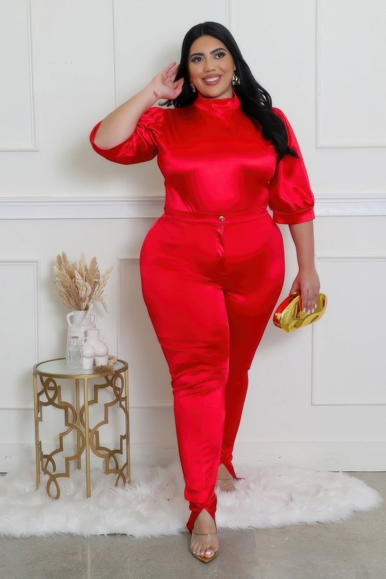 Woman wearing red sexy curvy two-piece satin bodysuit with high-waisted pants, standing confidently on a white rug.