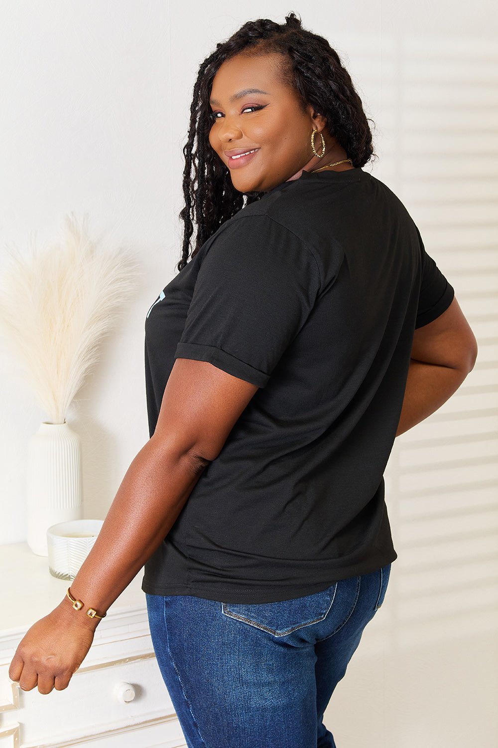 Woman wearing black slogan graphic cuffed sleeve t-shirt and blue jeans, showcasing comfortable and stylish fit.