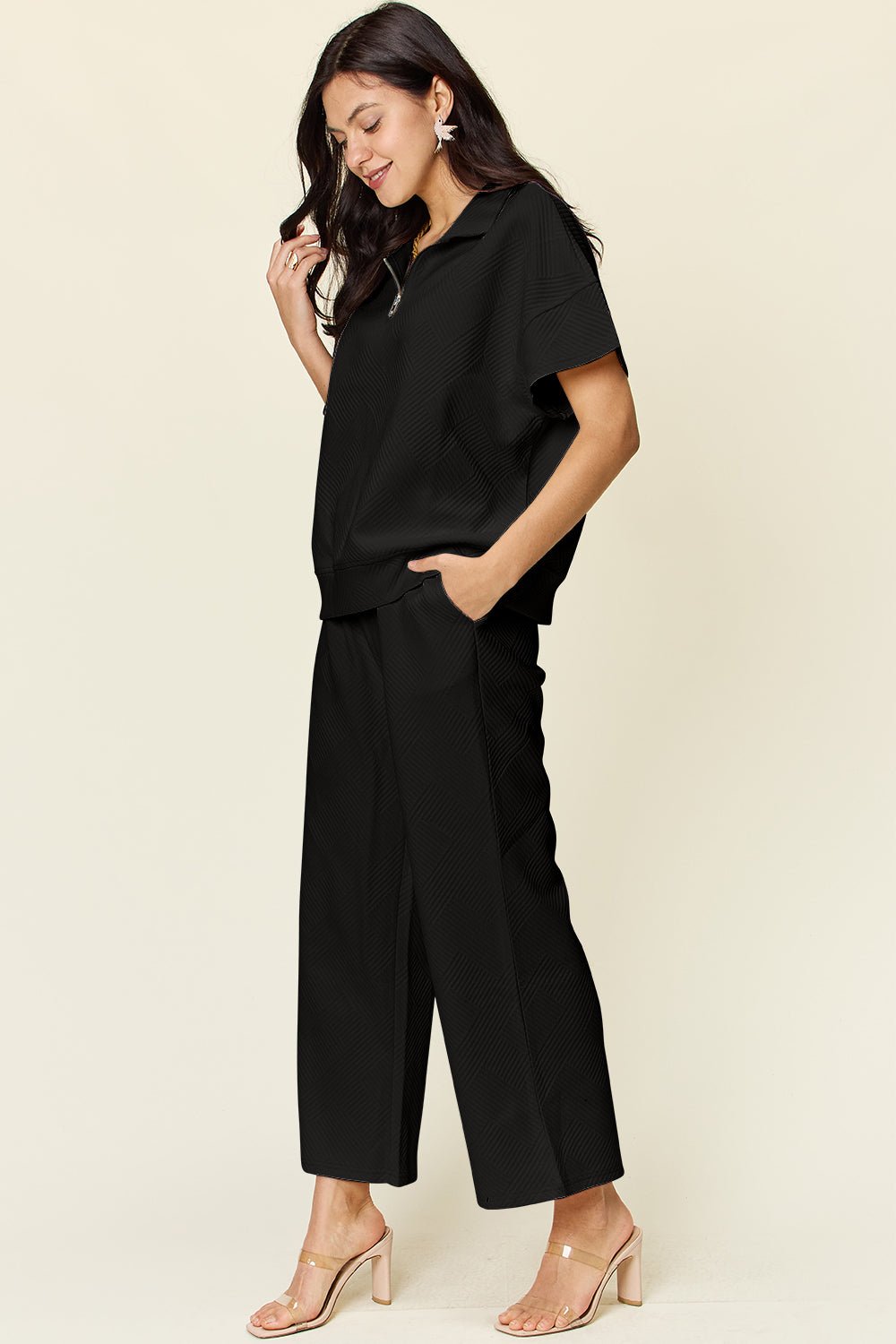 Woman wearing black half zip short sleeve top and pants set with pockets and drawstring, slightly stretchy fabric, polyester blend