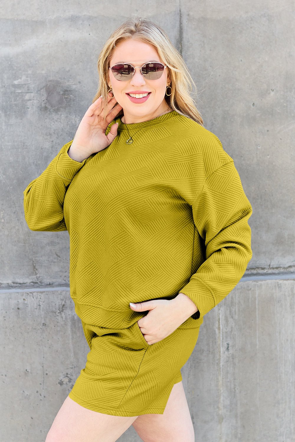 Woman wearing mustard textured long sleeve top and drawstring shorts set with pockets, posing against a concrete wall.