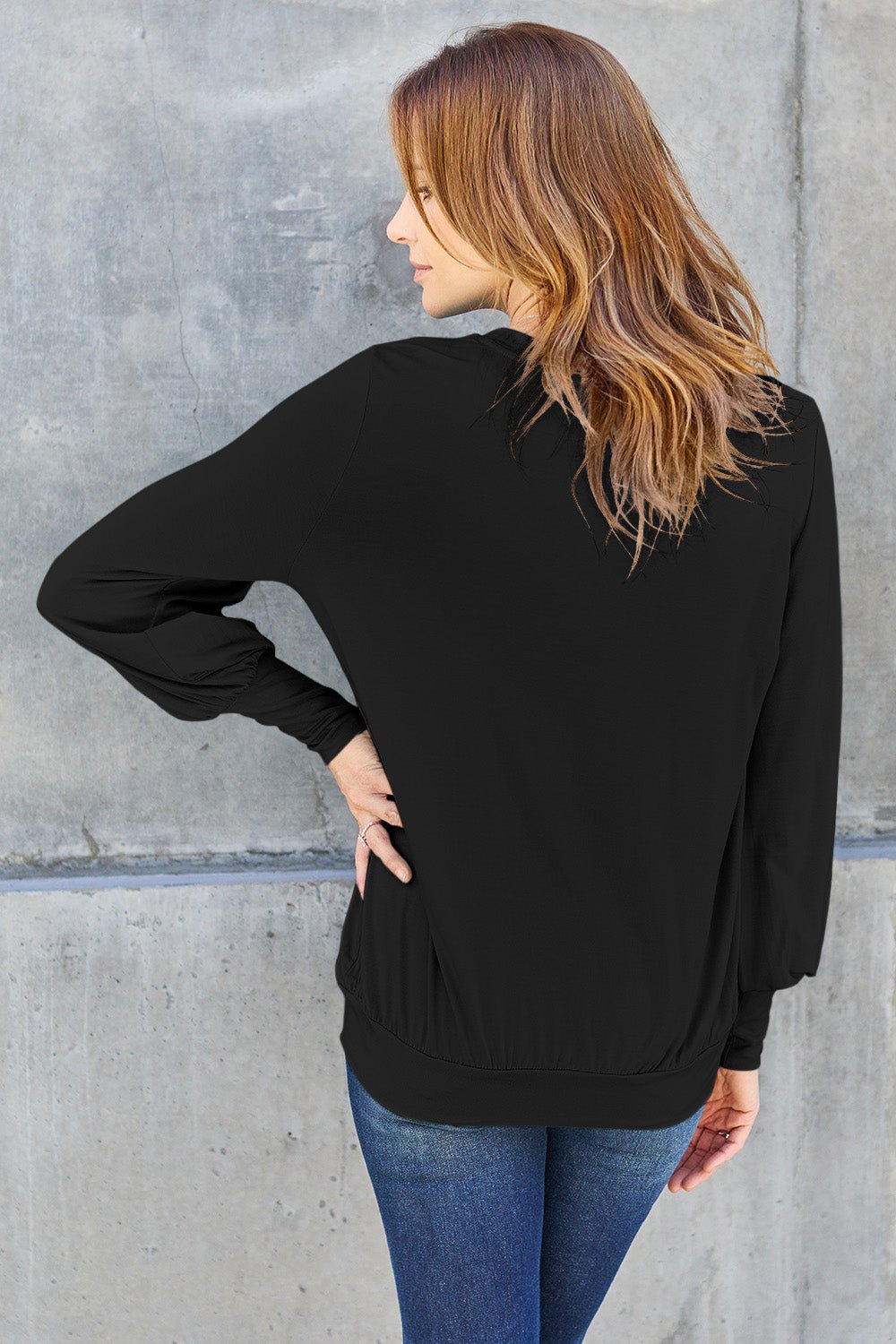 Woman wearing black V-neck lantern sleeve top with slightly stretchy rayon-spandex material, styled with blue jeans.
