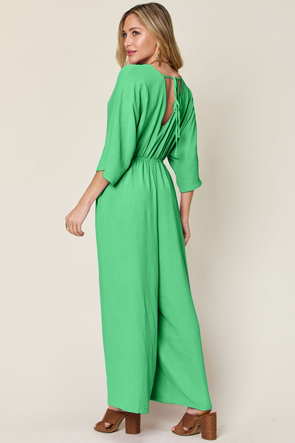 Green surplice wide leg jumpsuit with pockets and ruched tie-back design, made from polyester and spandex blend.