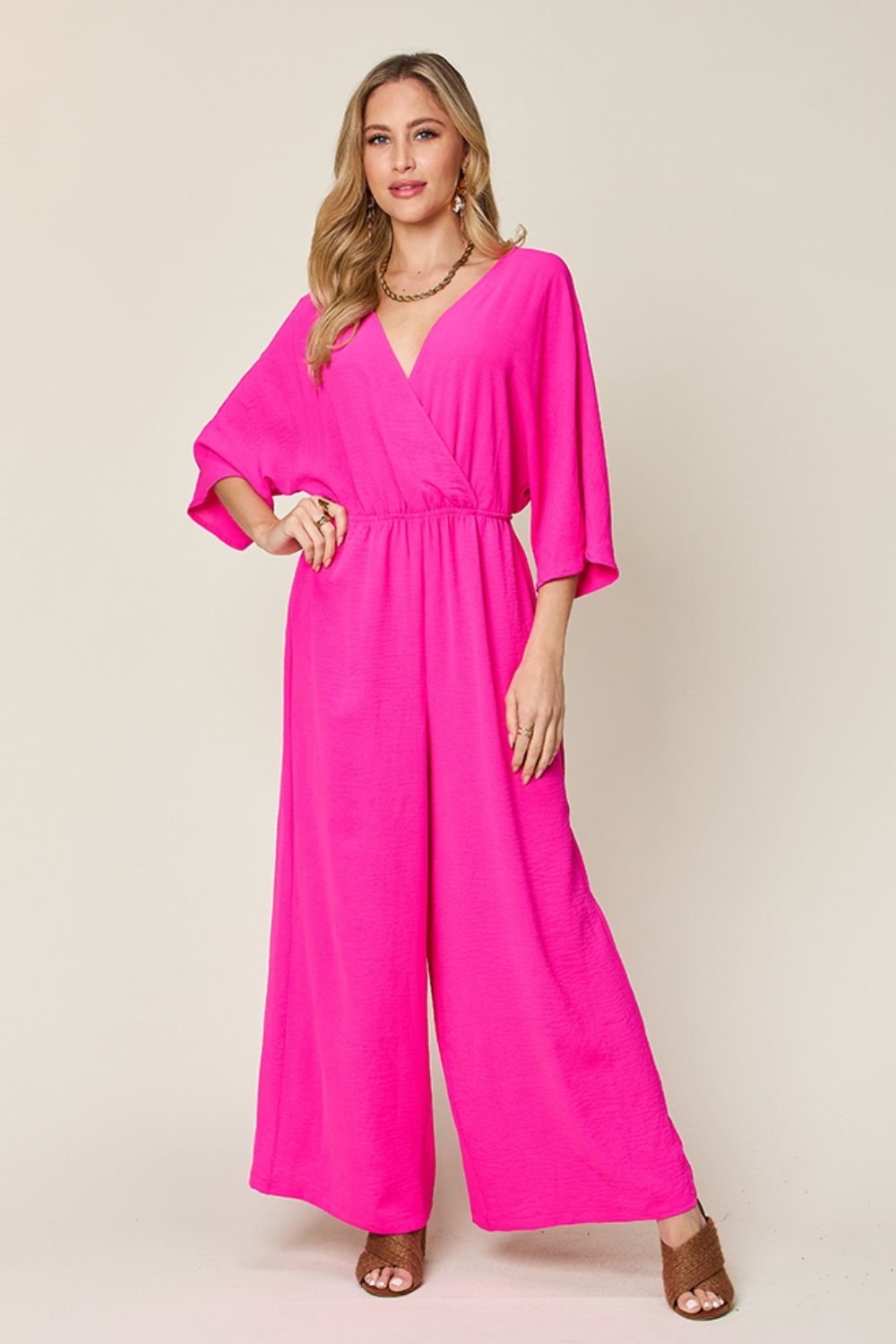 Surplice wide leg jumpsuit with pockets, vibrant pink, tied and ruched design, opaque polyester-spandex blend.