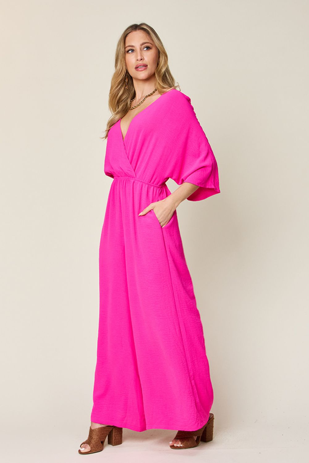 Bright pink surplice wide leg jumpsuit with pockets, featuring a tied and ruched design, worn by a model.