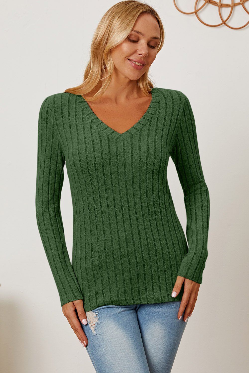 Woman wearing green ribbed V-neck long sleeve t-shirt, showcasing basic style and slight stretch, paired with light blue jeans.