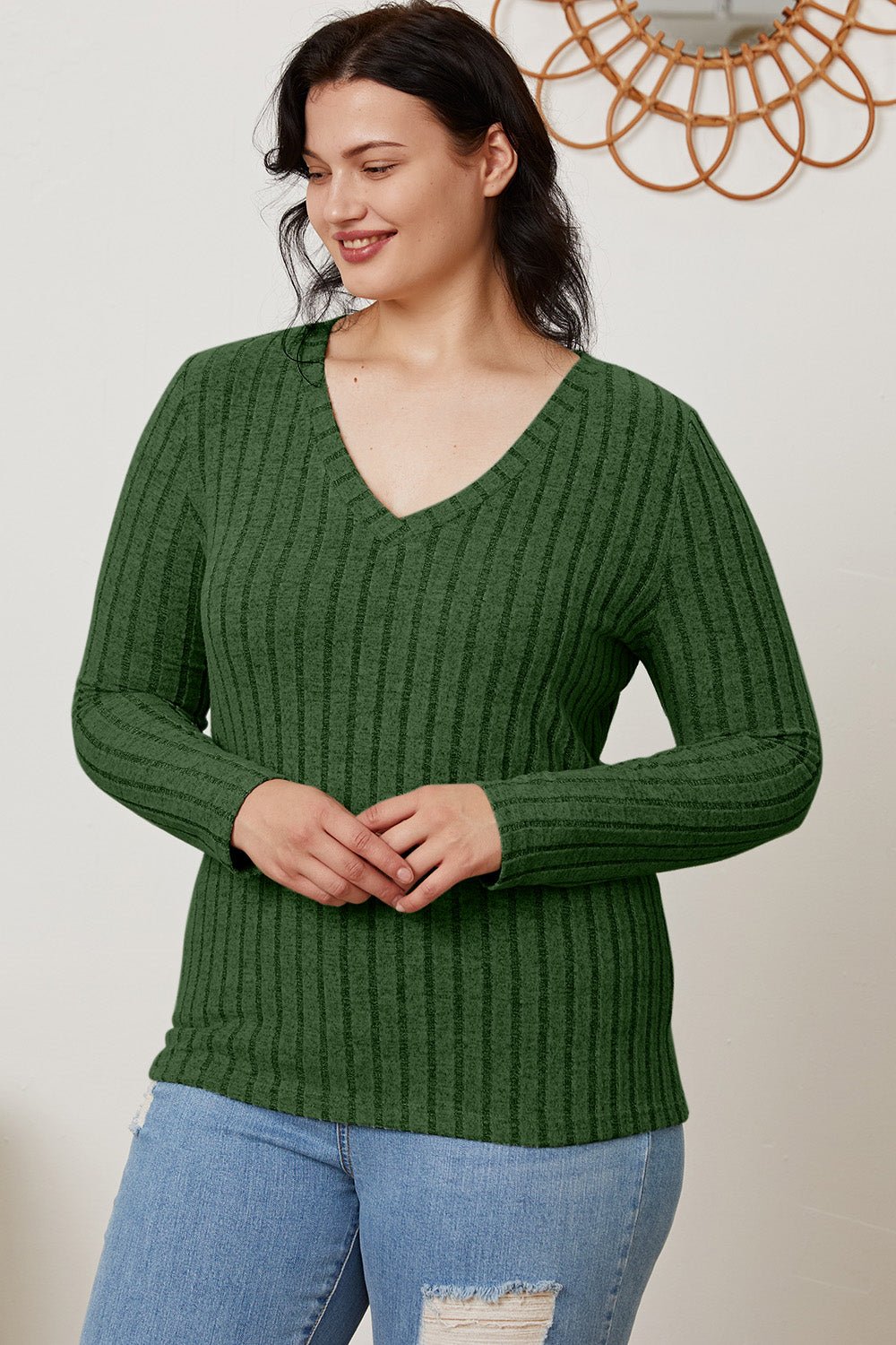 Woman in green ribbed V-neck long sleeve T-shirt and jeans, smiling, showcasing casual fashion.