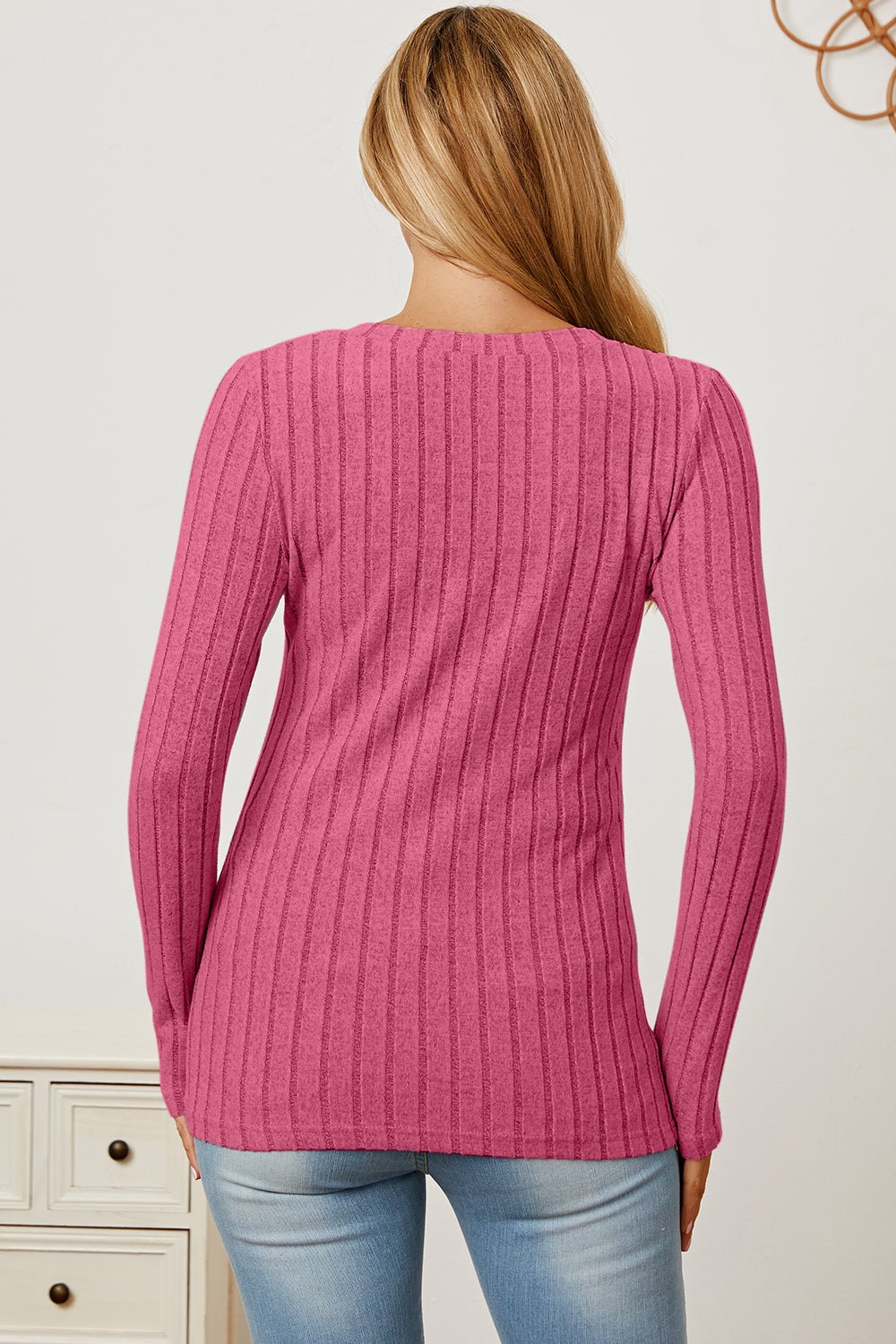 Woman wearing pink ribbed V-neck long sleeve T-shirt and jeans, showcasing the back view.
