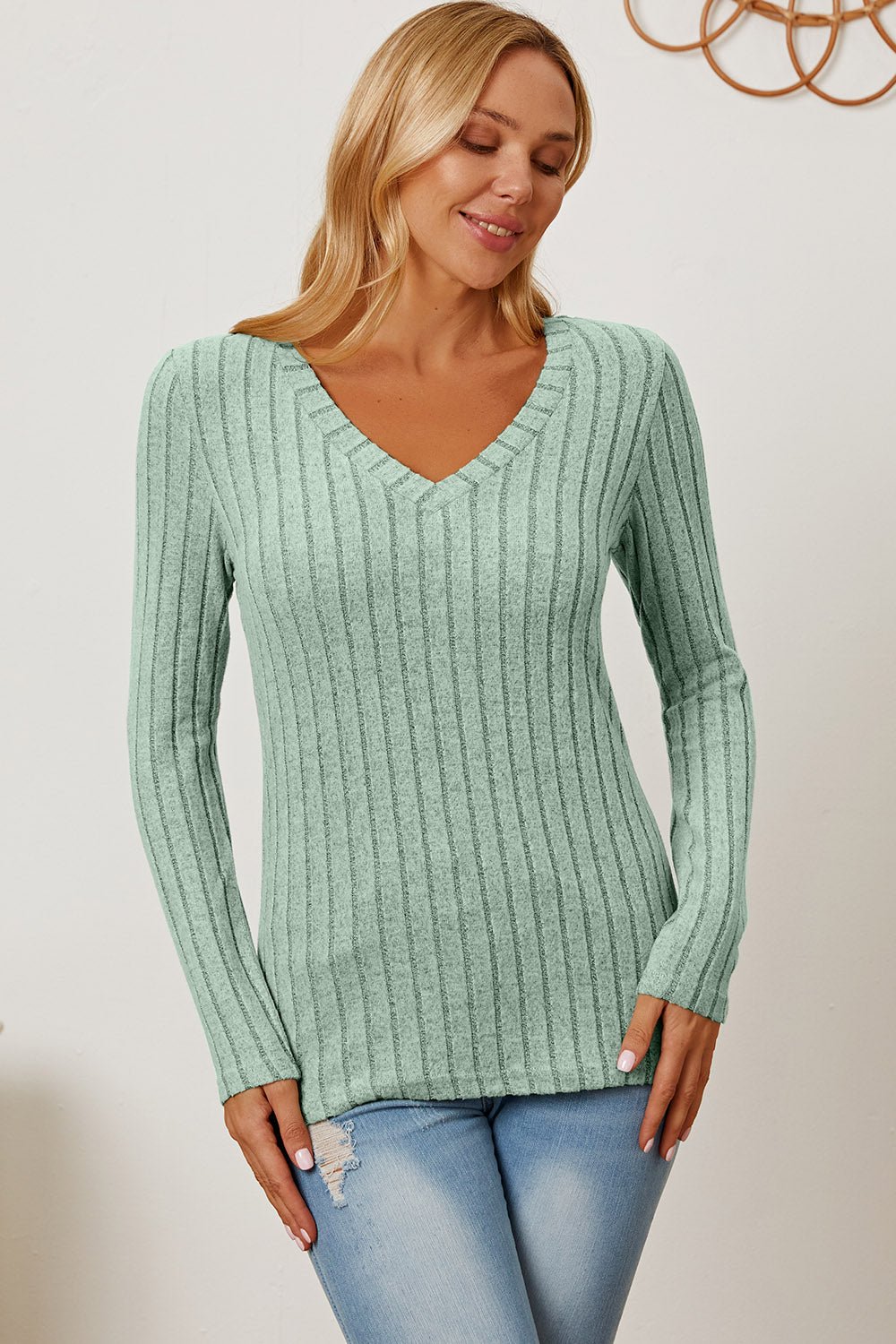 "Model wearing Basic Bae Full Size Ribbed V-Neck Long Sleeve T-Shirt in sage green paired with distressed jeans"