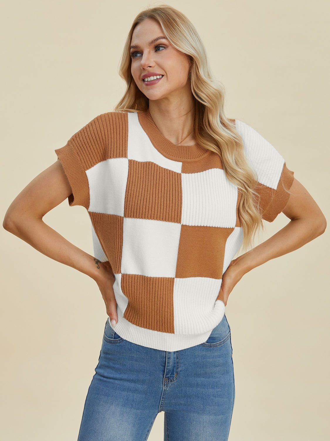 Woman wearing a checkered round neck short sleeve sweater in brown and white, paired with jeans.