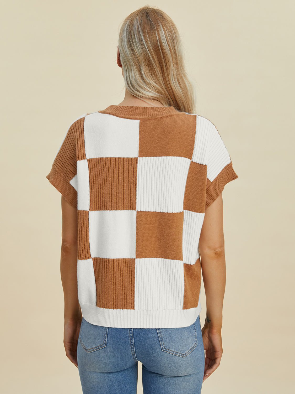Woman wearing a checkered round neck short sleeve sweater in brown and white, showcasing back design, paired with blue jeans.