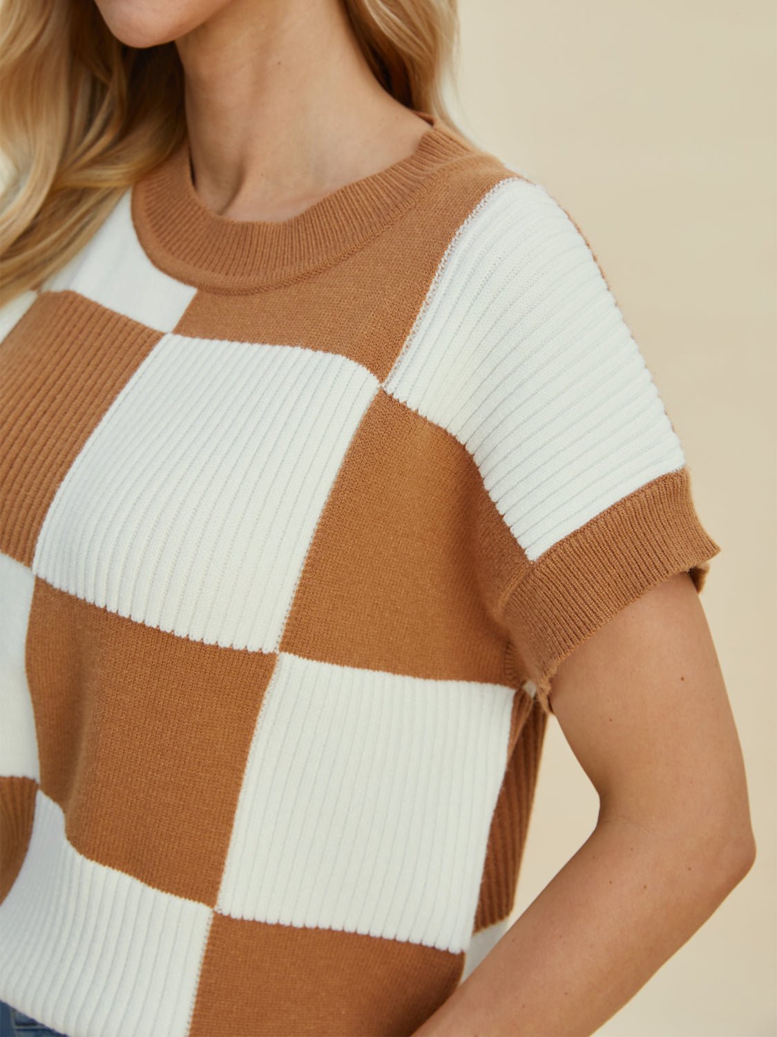 Woman wearing a checkered round neck short sleeve sweater in brown and white, featuring a slightly stretchy fabric.