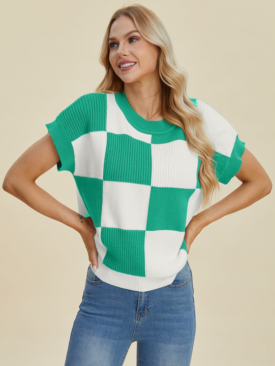 Woman wearing a checkered round neck short sleeve sweater in green and white, styled with blue jeans.