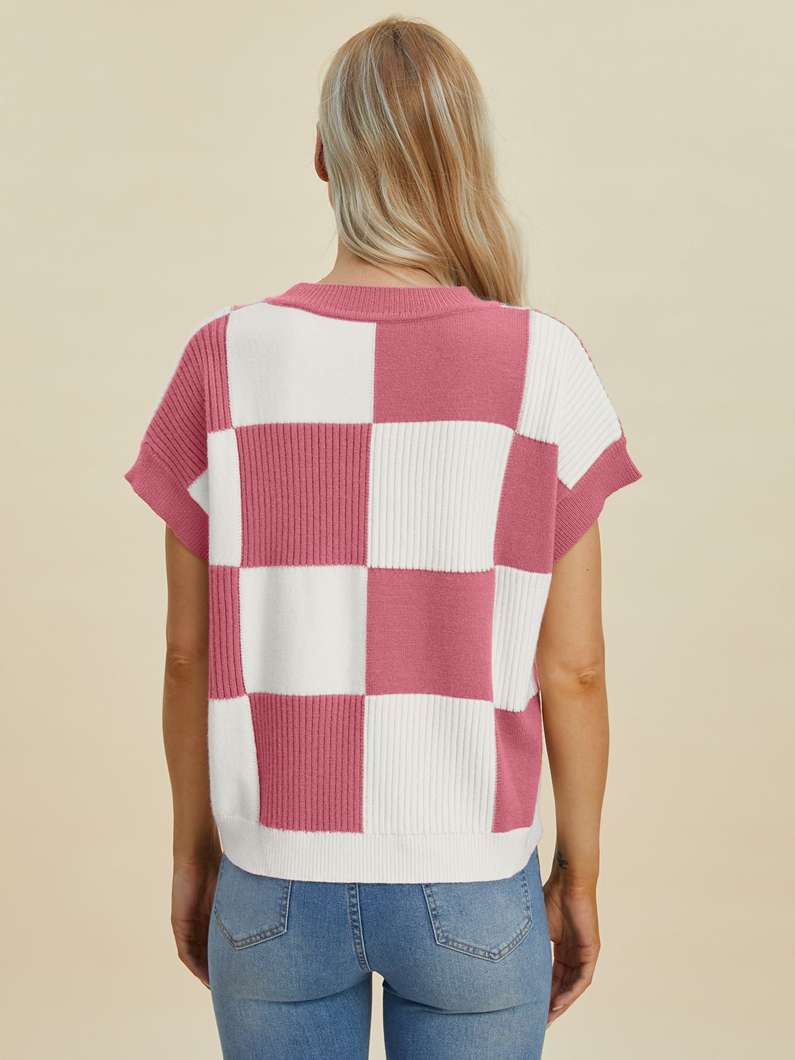 Woman wearing checkered round neck short sleeve sweater in pink and white, back view, slightly stretchy fabric.