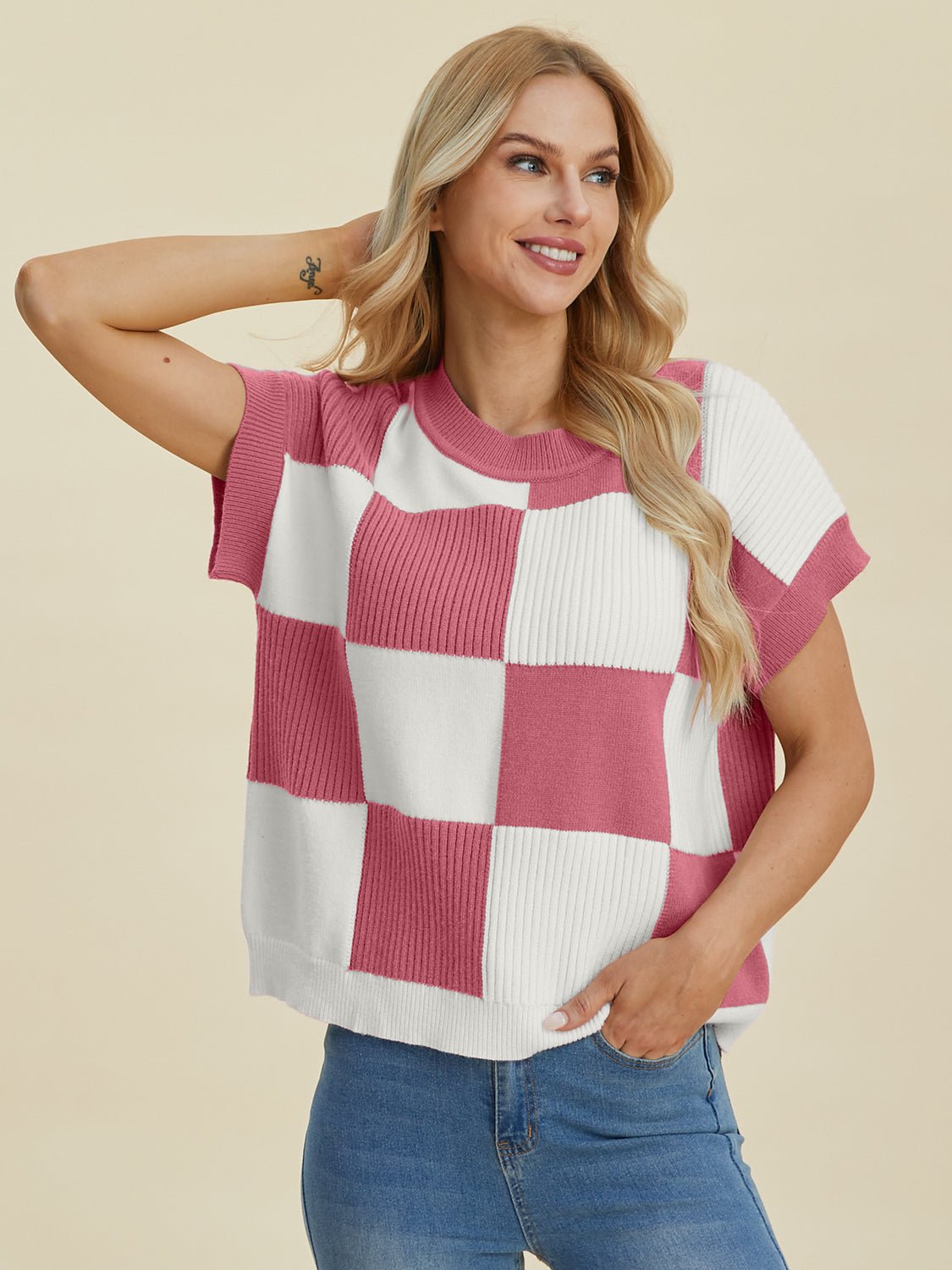 Woman wearing checkered round neck short sleeve sweater in pink and white with slightly stretchy fit, composed of viscose, polyester, and polyamide.