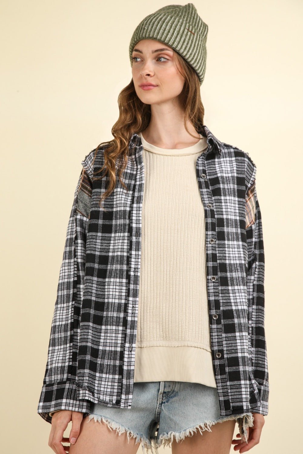 Woman wearing contrast plaid raw detail shirt with oversized fit in black, paired with a beanie and casual shorts.