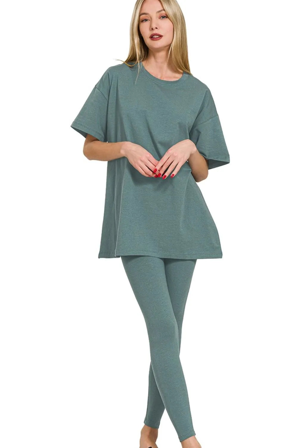 Woman in sage green matching loungewear set with oversized short-sleeve top and fitted leggings, standing against white background with hands...