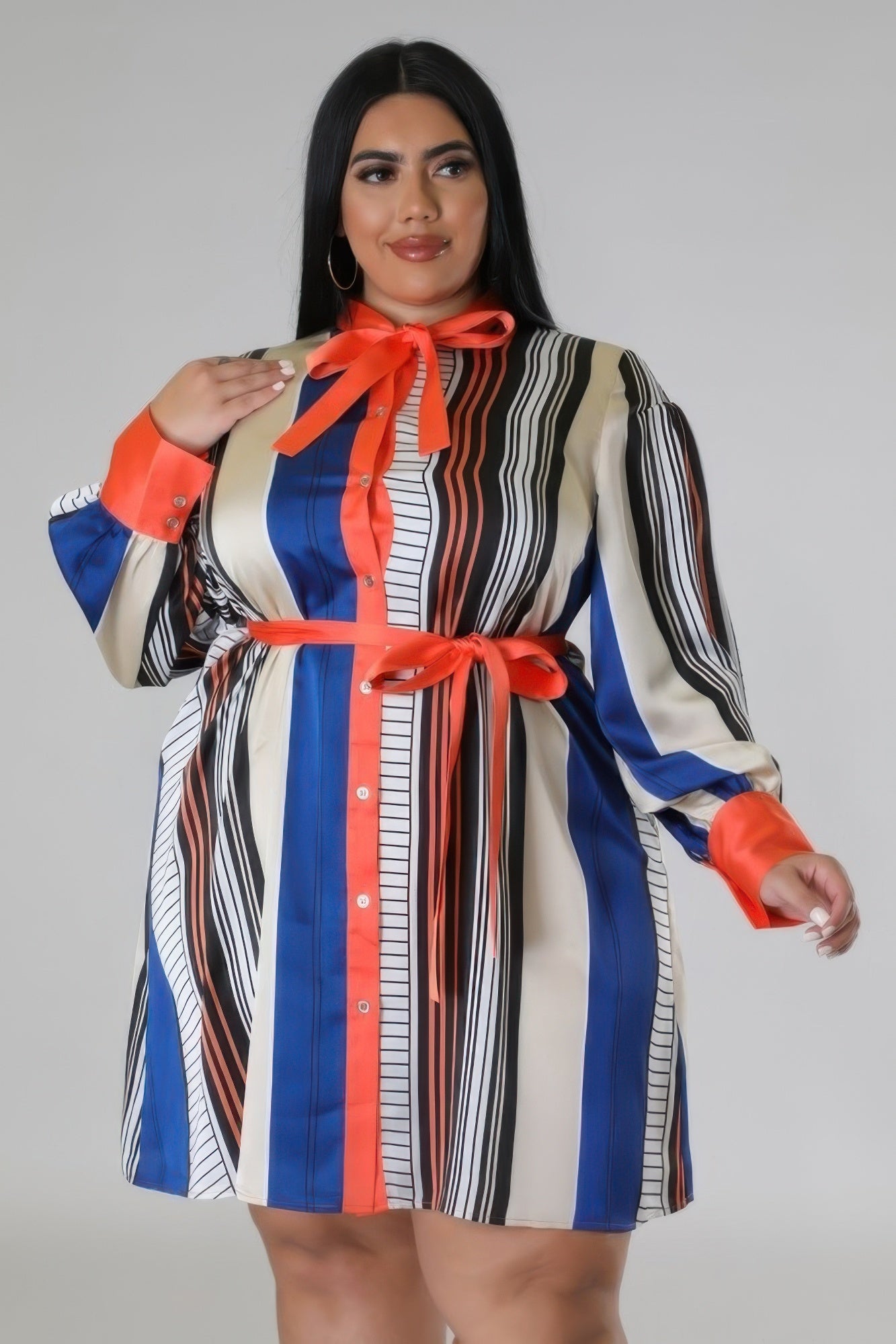 Curvy model wearing a colorful long sleeve non-stretch dress with vibrant stripes and a red bow belt, showcasing a chic plus-size fashion style.