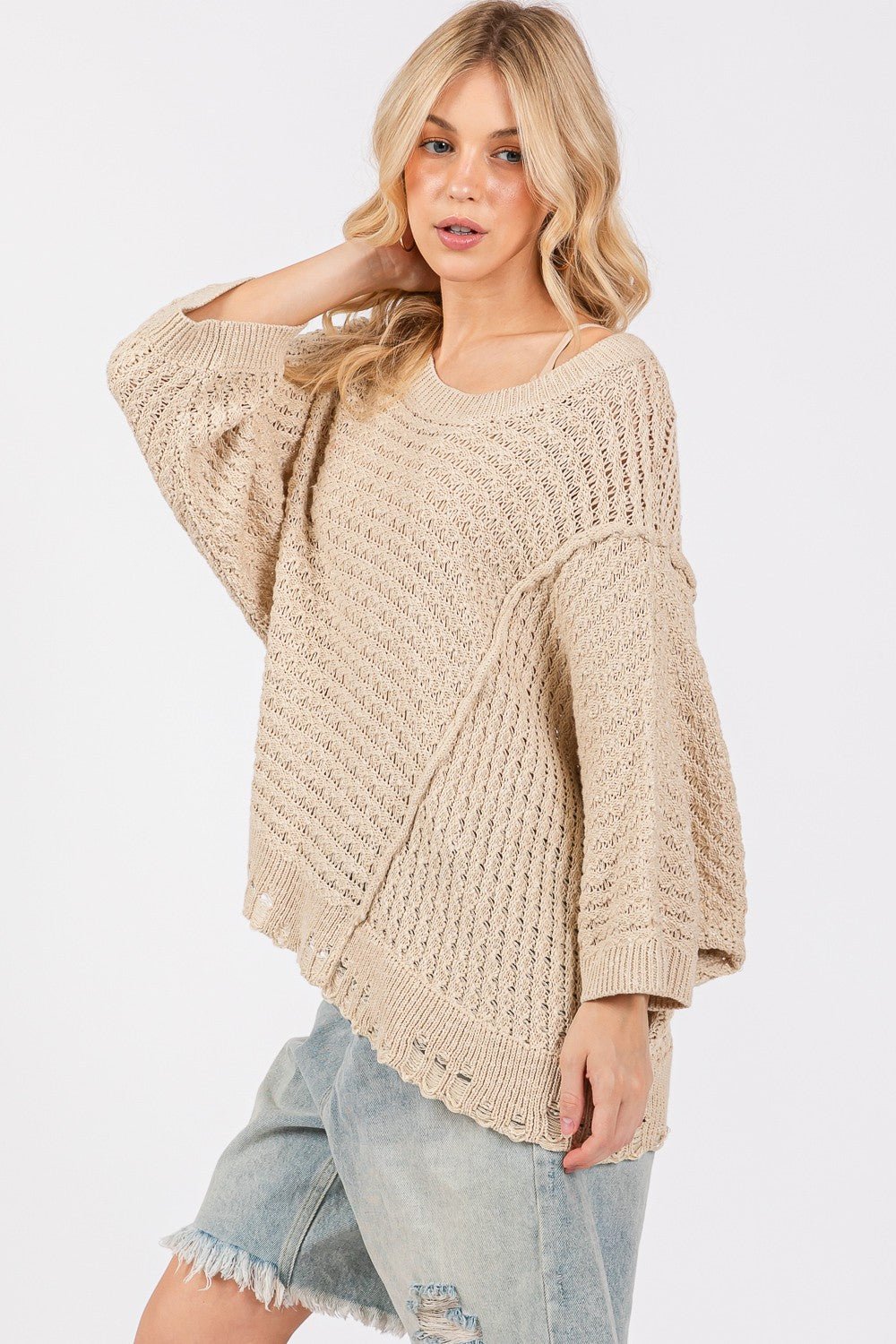 Woman wearing a distressed asymmetrical open stitch sweater, showcasing a casual look with slightly stretchy cotton-acrylic blend.