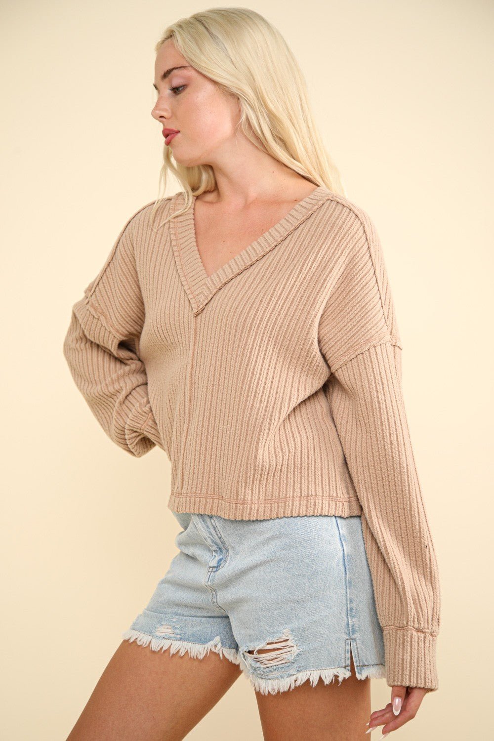 Woman wearing exposed seam V-neck ribbed knit top with slightly stretchy cotton blend, paired with distressed denim shorts.