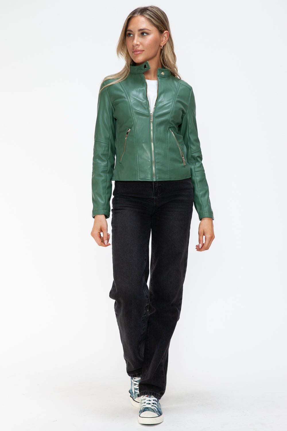 Woman wearing a green faux leather zip-up jacket with a drawstring hood and pockets, styled with black jeans and sneakers.