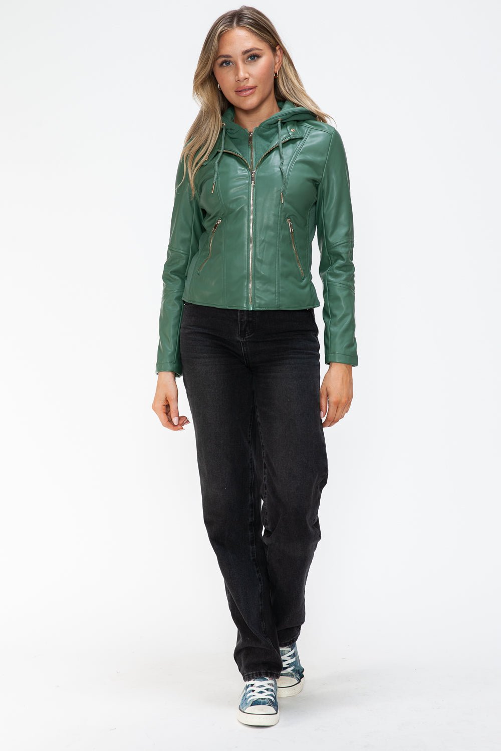 Woman wearing green faux leather zip up drawstring hooded jacket with pockets, paired with black jeans and sneakers.