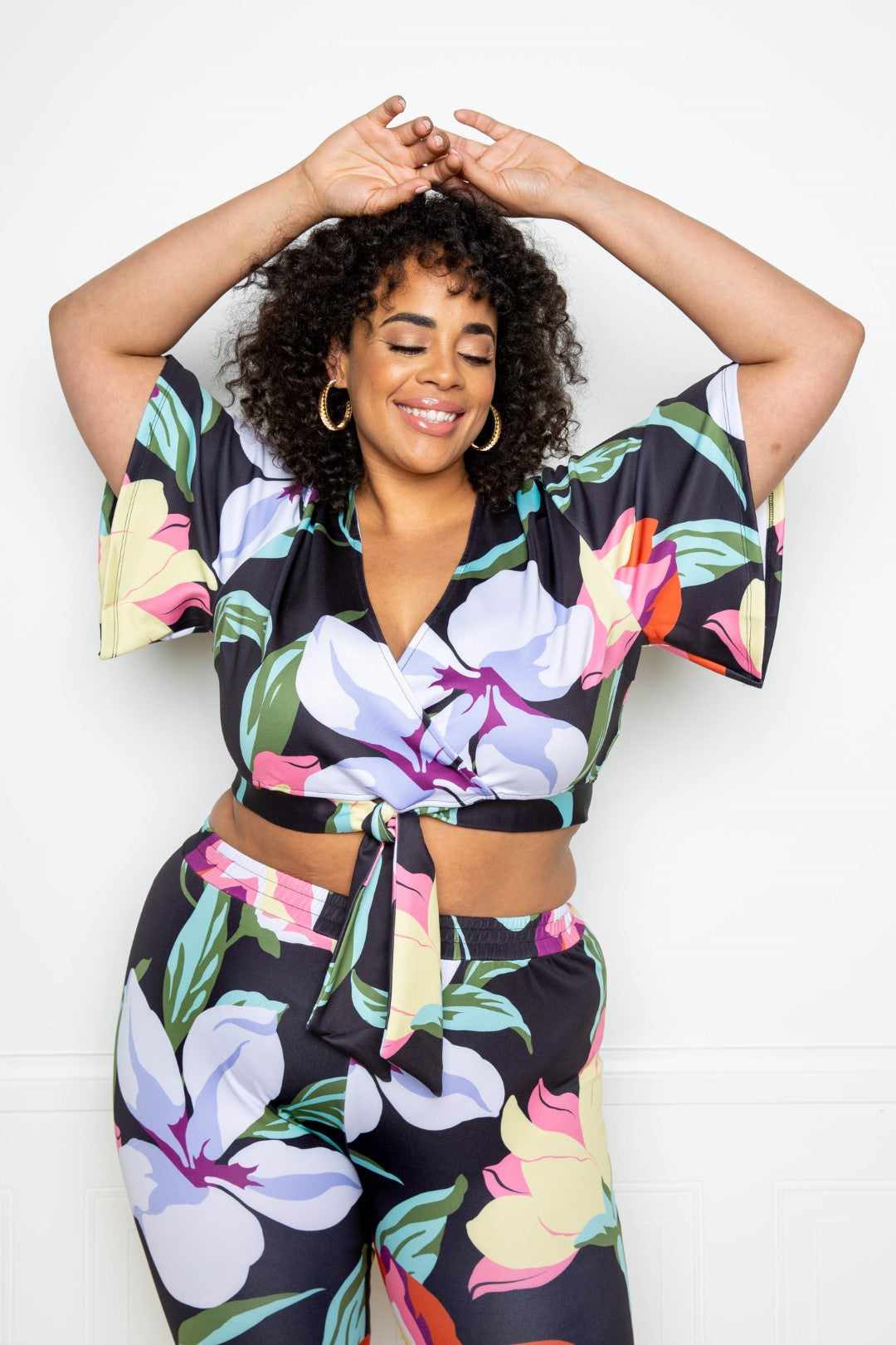 Woman wearing multi-colored flower jogger and top set in plus size, featuring a vibrant floral design on black background.