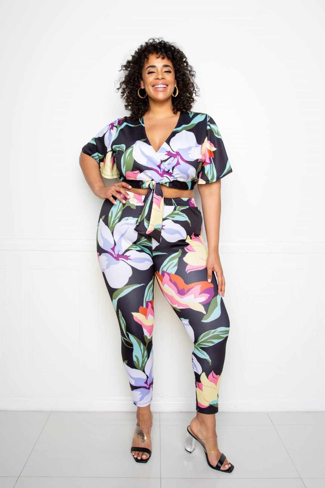 Plus-size model in a vibrant multi/black flower jogger and top set made from polyester and spandex, perfect for fashionable comfort.