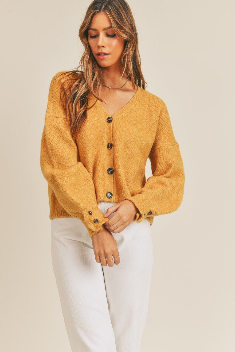 Woman wearing a mustard long sleeve button down sweater cardigan made of acrylic, polyester, and spandex, slightly stretchy material.