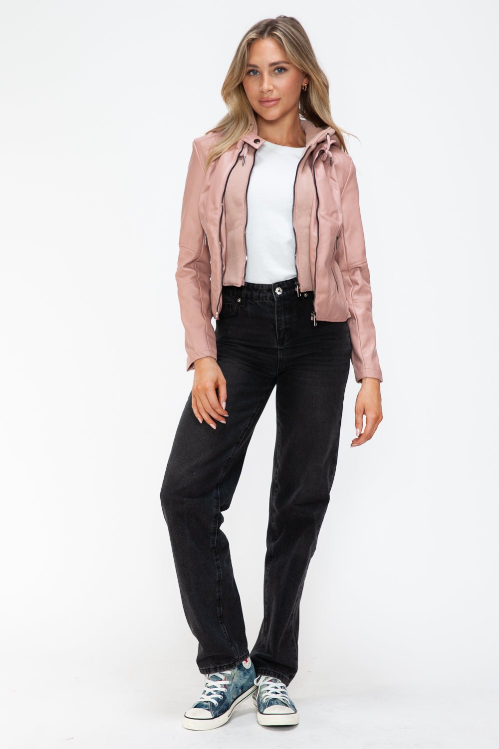 Woman wearing mauve faux leather zip-up drawstring hooded jacket, white top, and black jeans with sneakers.