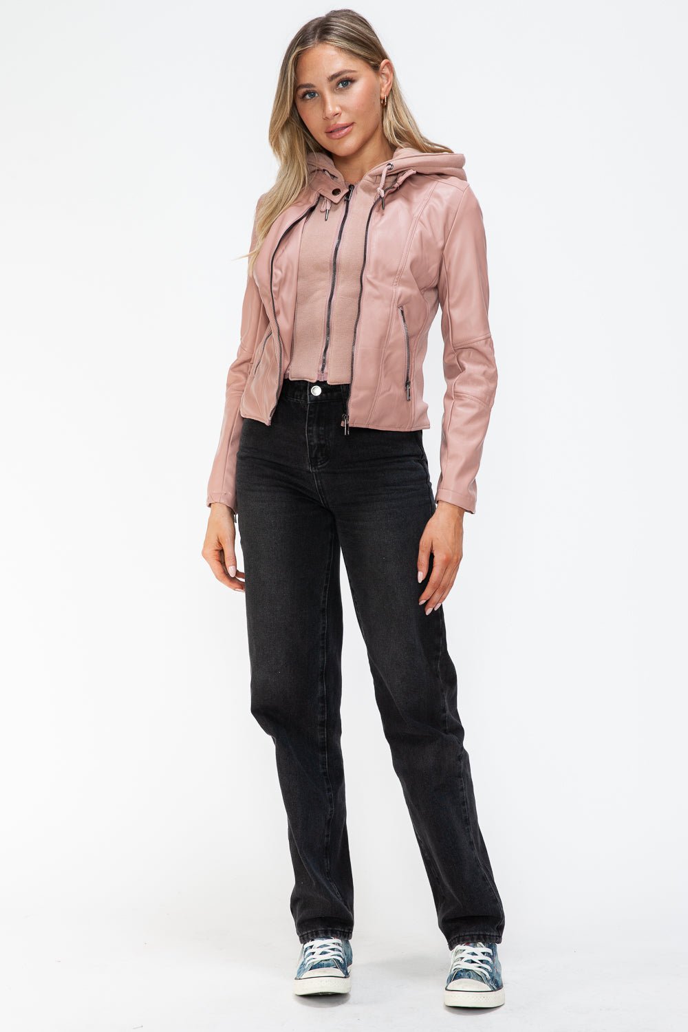 Woman wearing mauve faux leather zip-up drawstring hooded jacket with black jeans and sneakers.